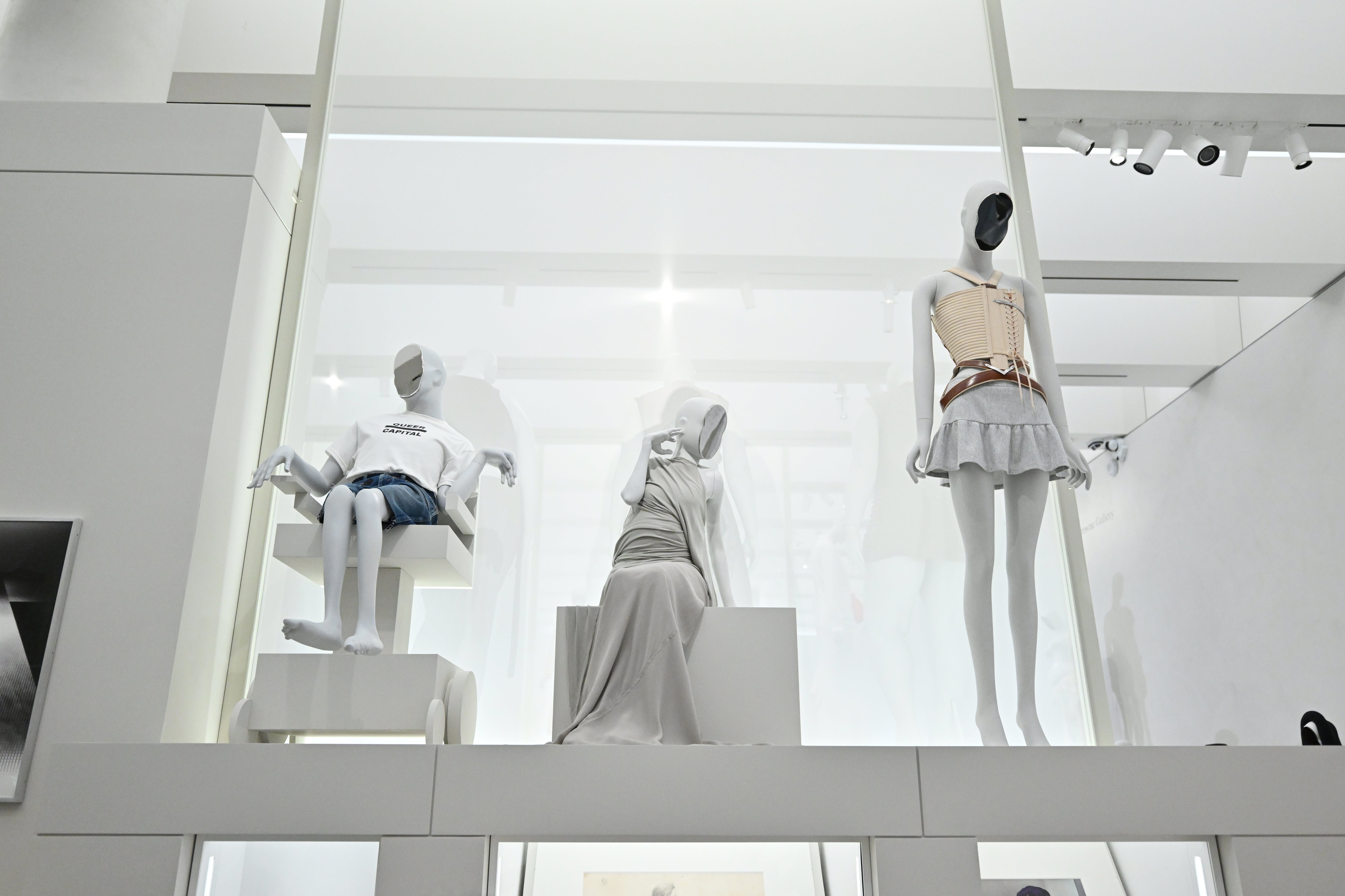 Three mannequins show  modern, minimalist outfits, including a casual T-shirt and shorts, a flowing dress, and a structured apical  with a skirt