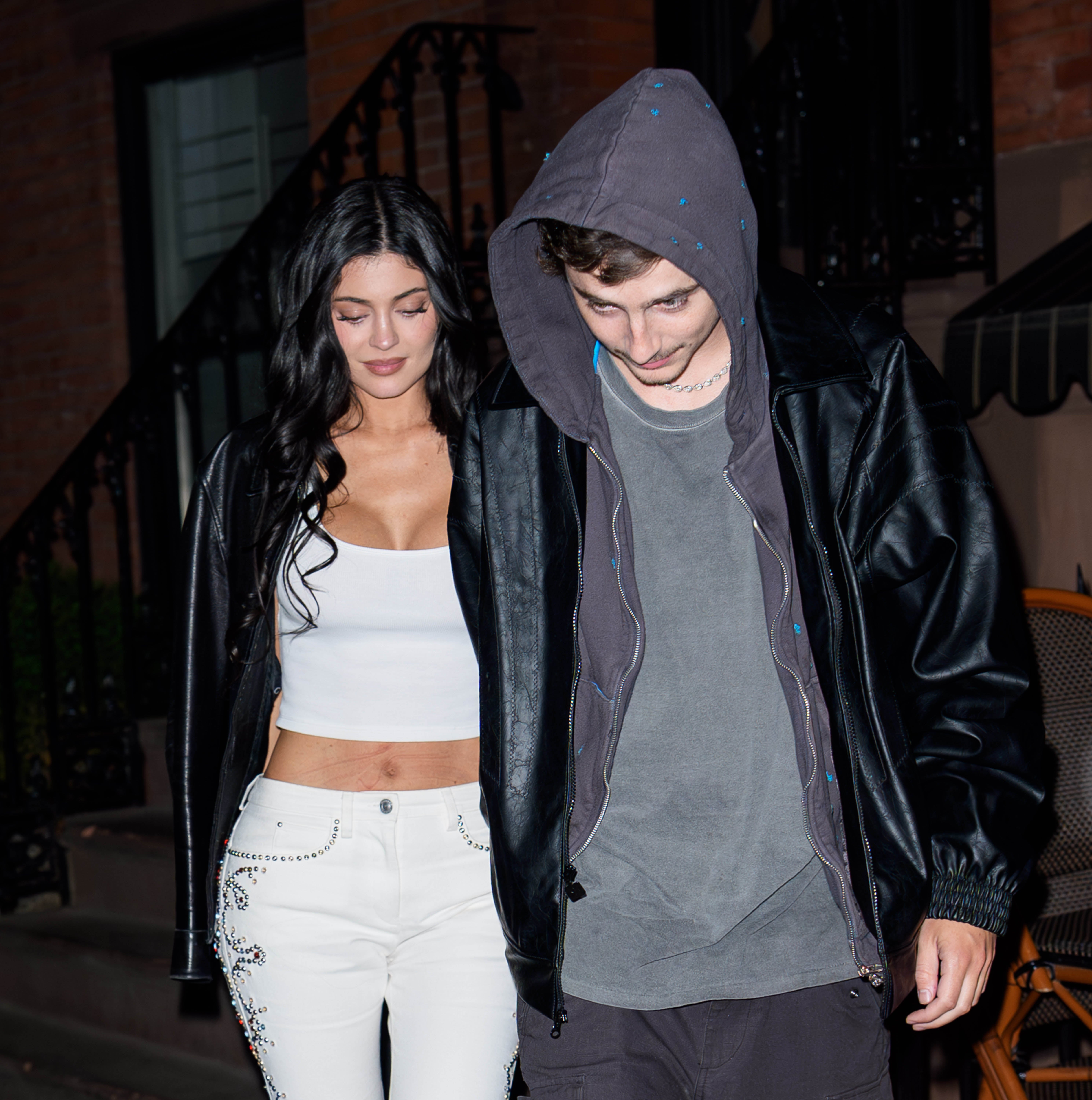Two radical   walking outdoors. The pistillate   wears a achromatic  apical  and jeans; the antheral   wears a hoodie and jacket