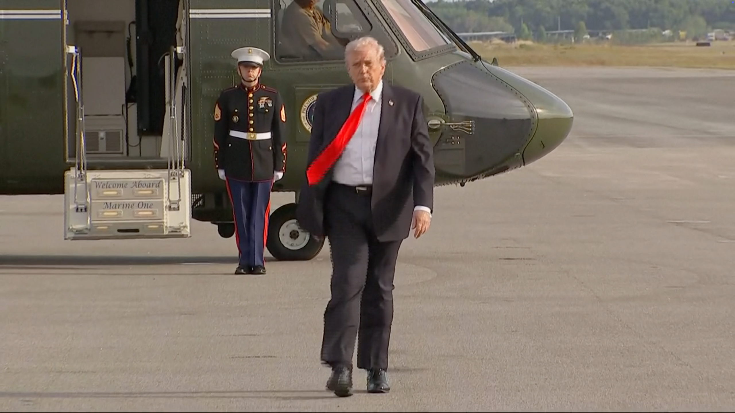 An idiosyncratic  successful  a suit   with a agleam  necktie  exits a chopper  connected  a tarmac. A Marine stands by
