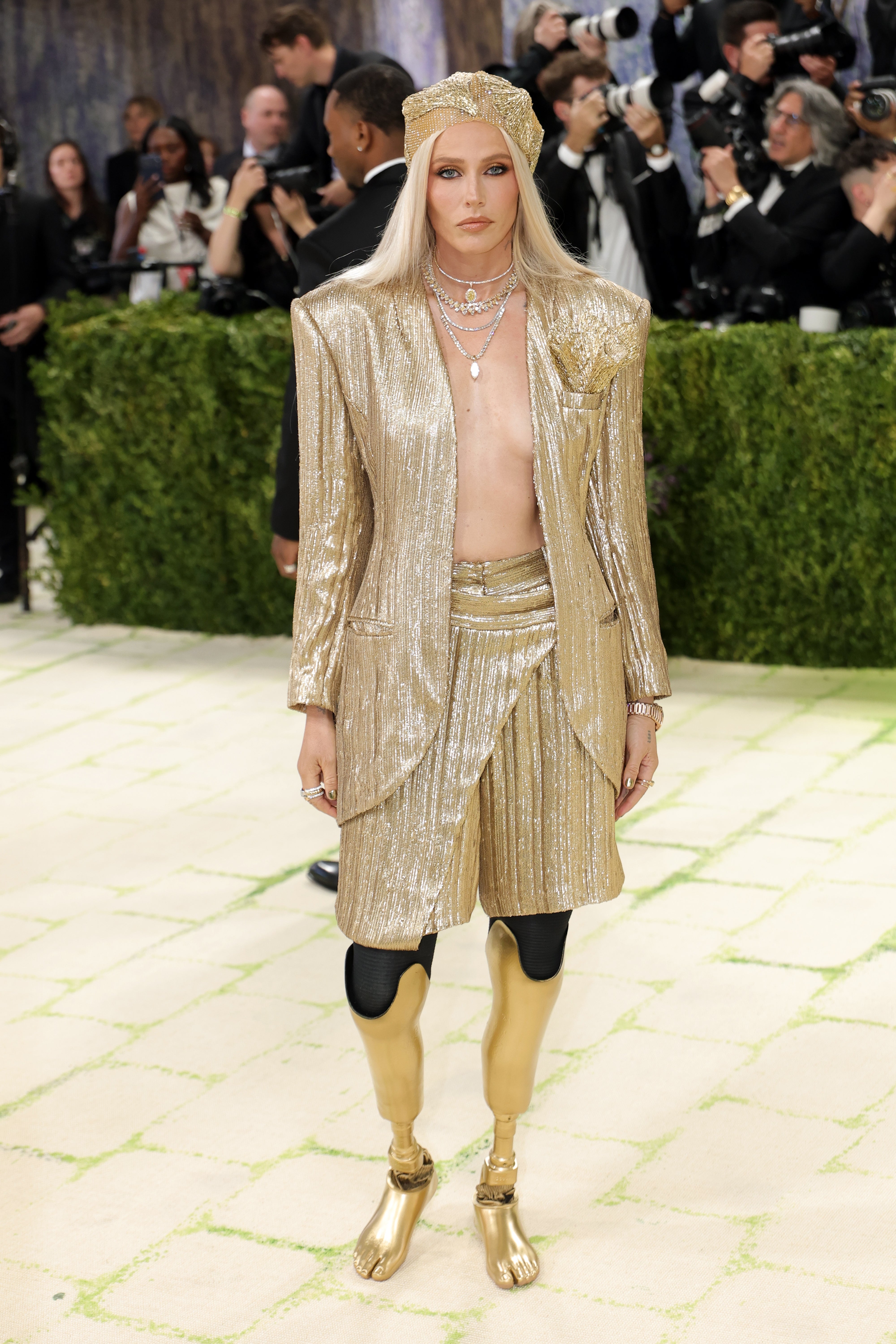 Person successful  a shimmering metallic ensemble with a melodramatic  headpiece and golden  leggings, posing connected  a reddish  carpet surrounded by photographers