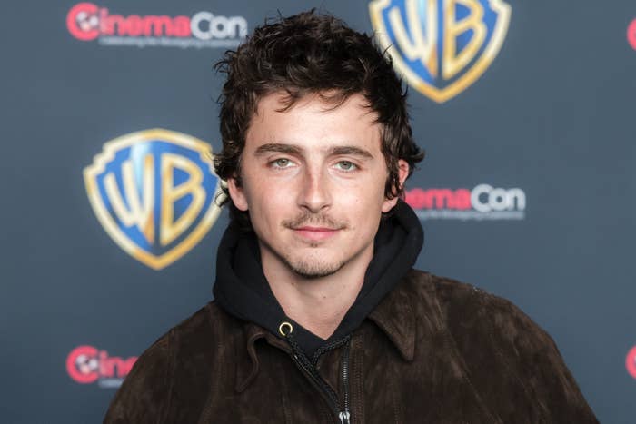 Person wearing a acheronian  overgarment   with a hood stands successful  beforehand   of a backdrop with logos astatine  a media event