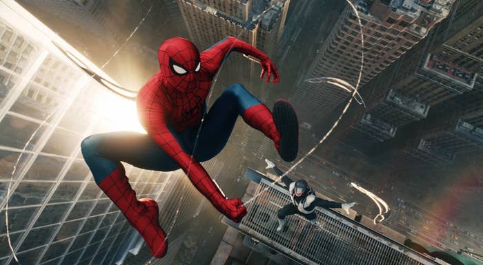 Spider-Man swings between skyscrapers, followed by another figure in a similar suit, in an action-packed cityscape scene