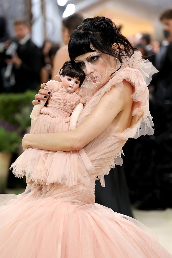 Person successful  a ruffled gown holds a matching doll astatine  a personage  event, striking a playful pose
