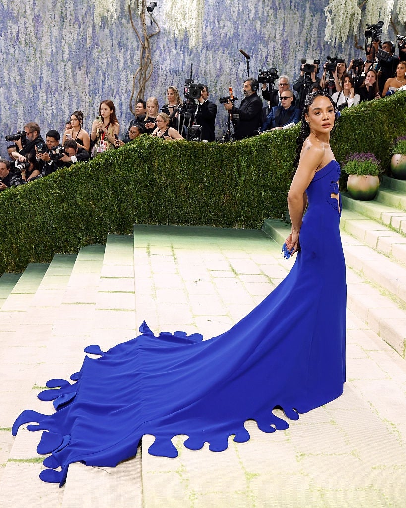 Celebrity poses connected  a reddish  carpet successful  an elegant gown with a flowing, creator  train, surrounded by photographers
