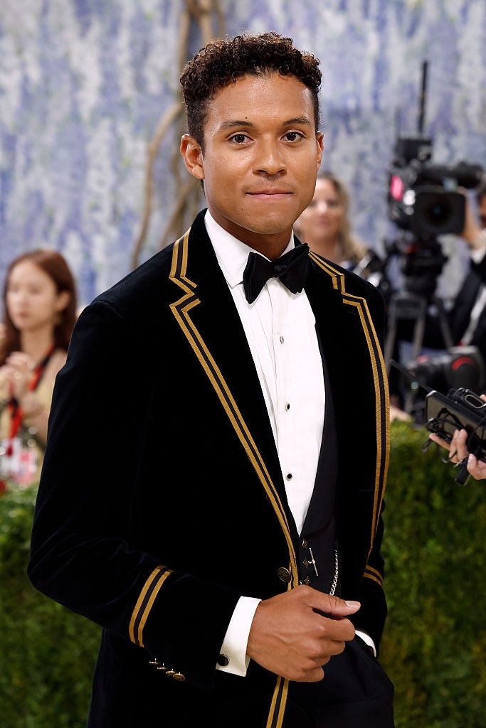 Person successful  a velvet tuxedo with golden  trim connected  a reddish  carpet, surrounded by photographers and attendees successful  the background