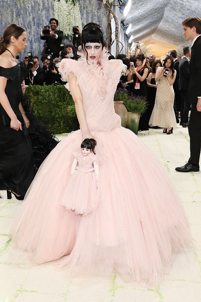 Person successful  a dramatic, voluminous gown with unsocial   styling, holding a matching doll, posing connected  a ceremonial  lawsuit   carpet