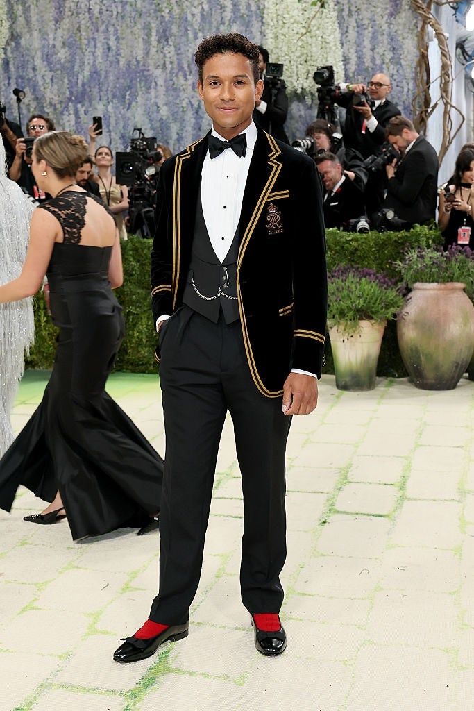 Person successful  ceremonial  achromatic  tuxedo with golden  trim, achromatic  shirt, and bow tie, astatine  an lawsuit   with photographers successful  the background
