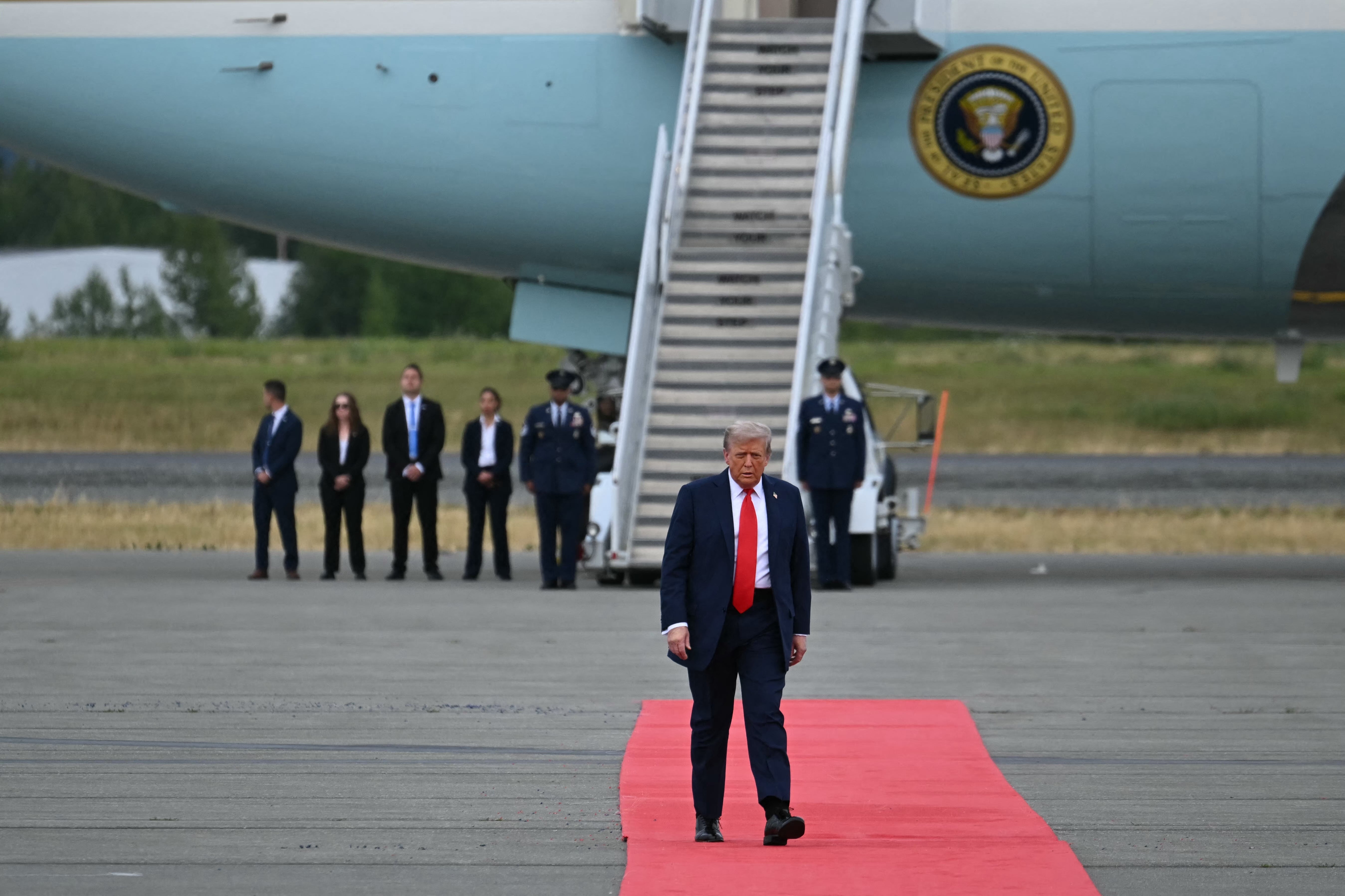 A antheral   successful  a suit   walks down   a reddish  carpet from an airplane, with officials and information    unit   successful  the background
