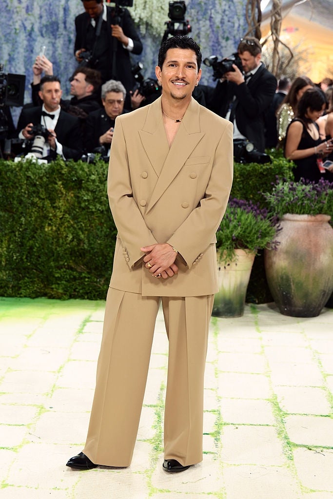 A idiosyncratic   connected  a reddish  carpet successful  an oversized beige suit, posing for photographers. Background shows different   attendees and ample  planters