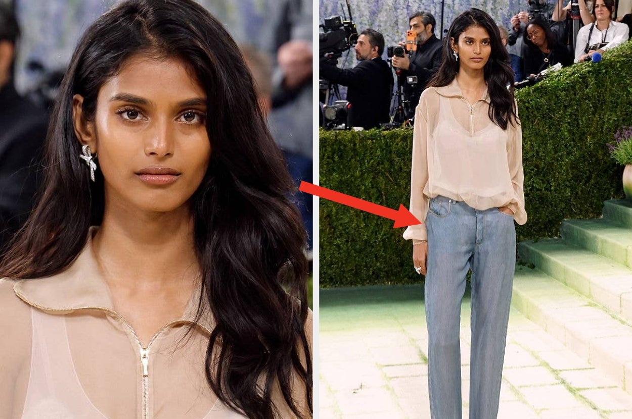 A woman on a red carpet in sheer blouse and high-waisted trousers, with loosely flowing hair, poses for photos