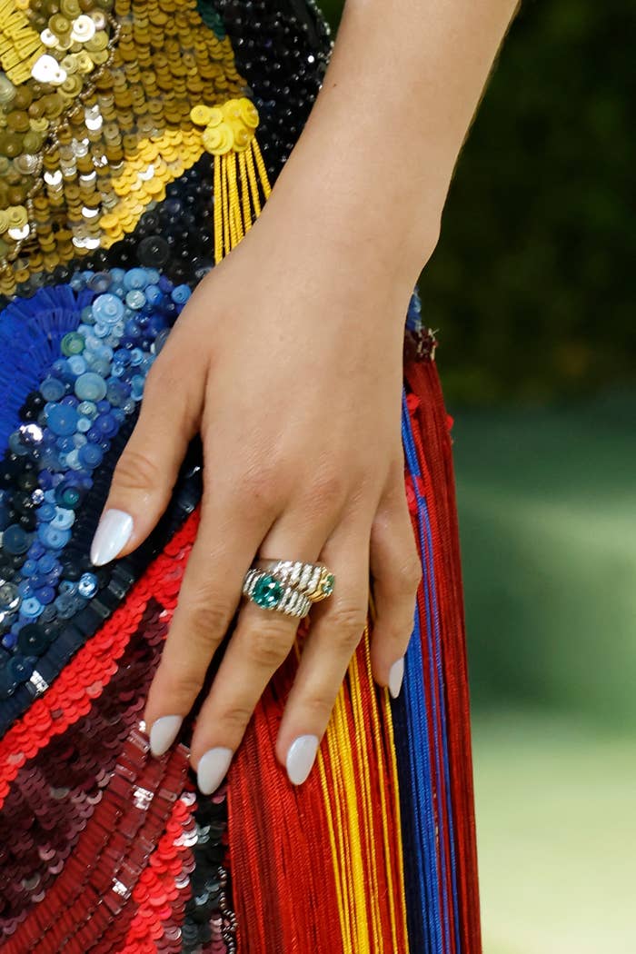 A manus  adorned with achromatic  polish and a jeweled ring, resting connected  a colorful, sequined and tasseled fabric
