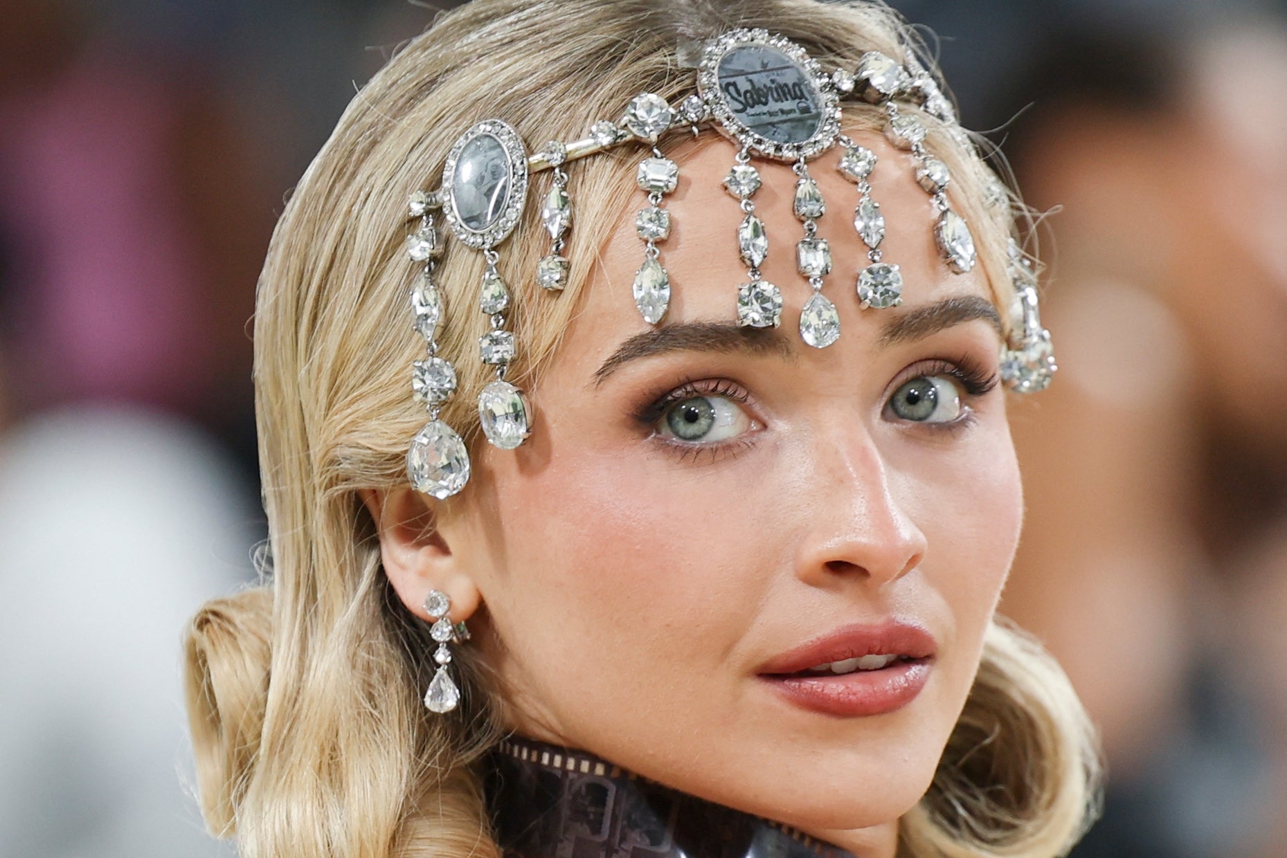 Person with jeweled headpiece featuring intricate designs and dangling gems, looking towards the camera