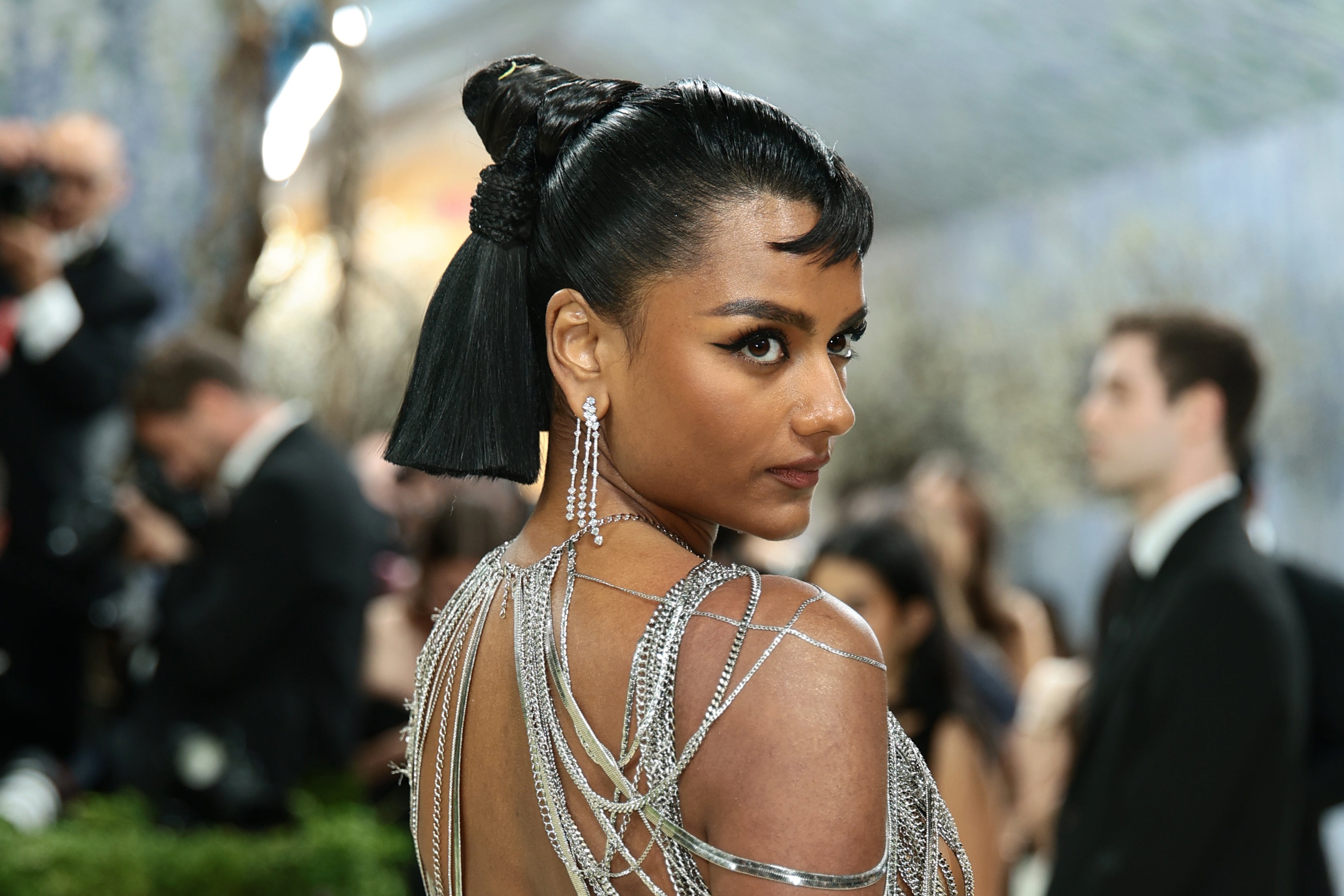 Person successful  elegant formal  with shimmering concatenation  details, posing astatine  an event. Hair styled successful  a bun with a fringe
