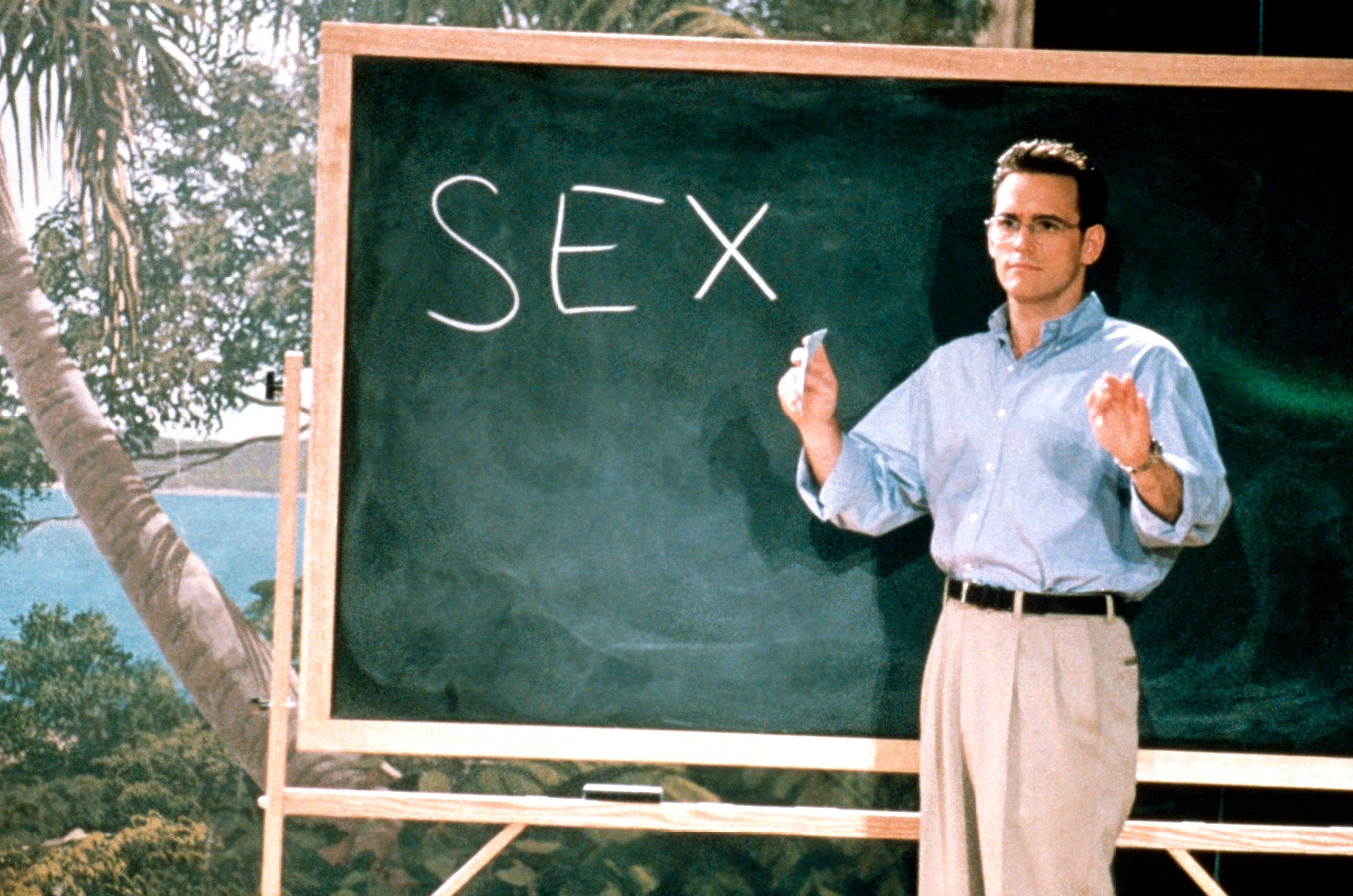 Person standing next to a chalkboard with "SEX" written on it, appearing to teach or present