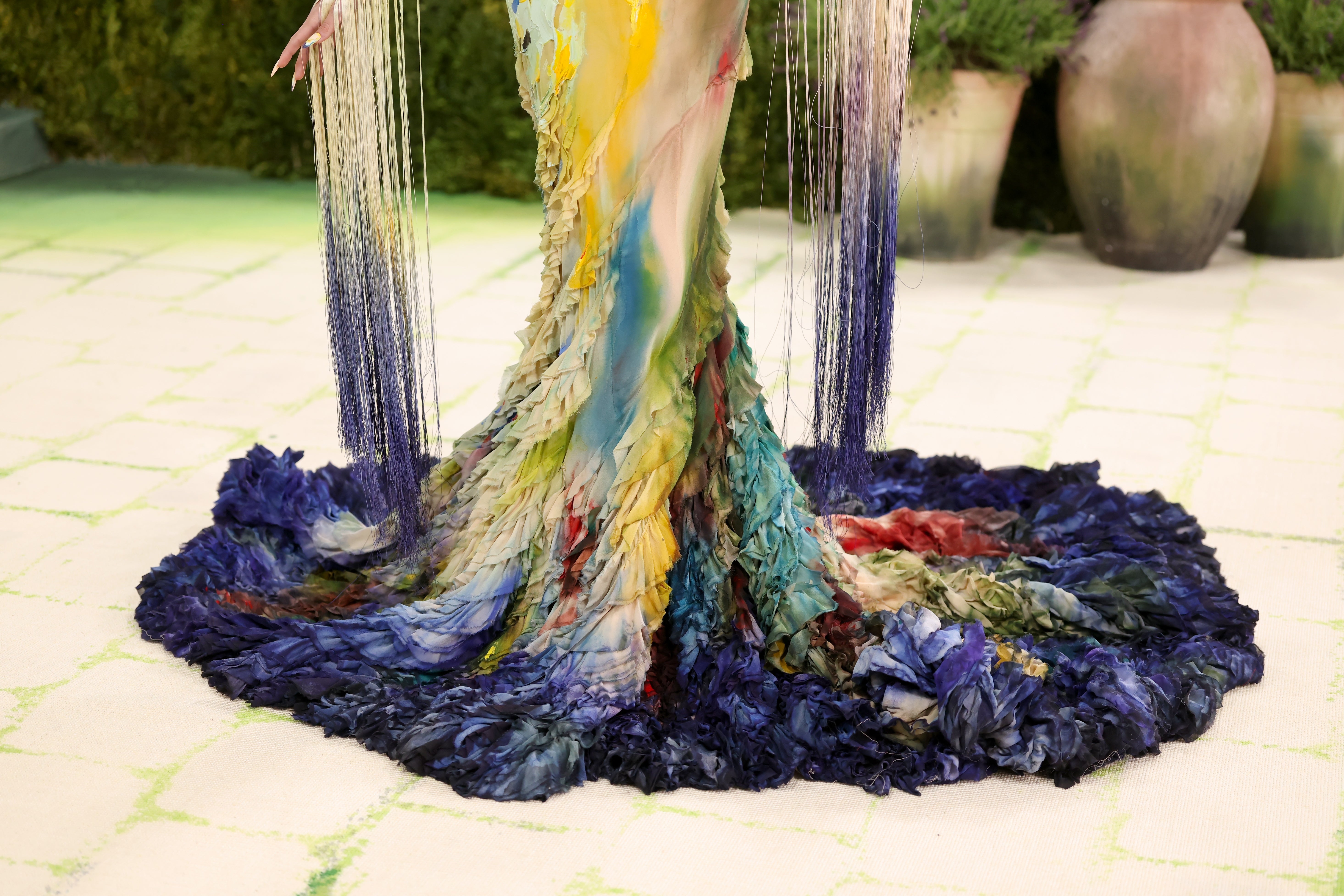 Person wearing a melodramatic  textured gown with a flowing, feathered, and multicolored plan  astatine  the hem connected  a patterned floor