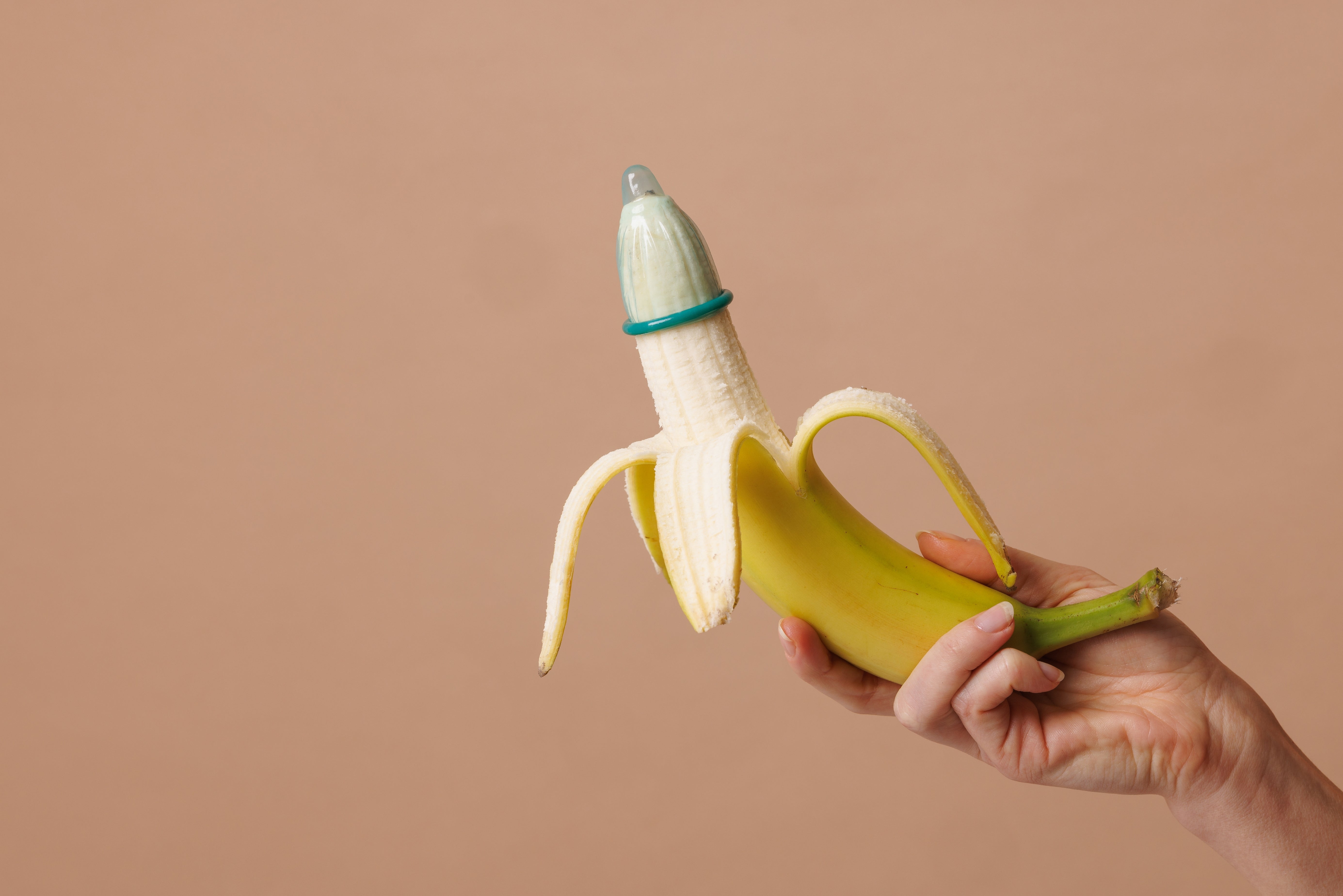 Hand holding a peeled banana with a condom on the tip, illustrating safe sex