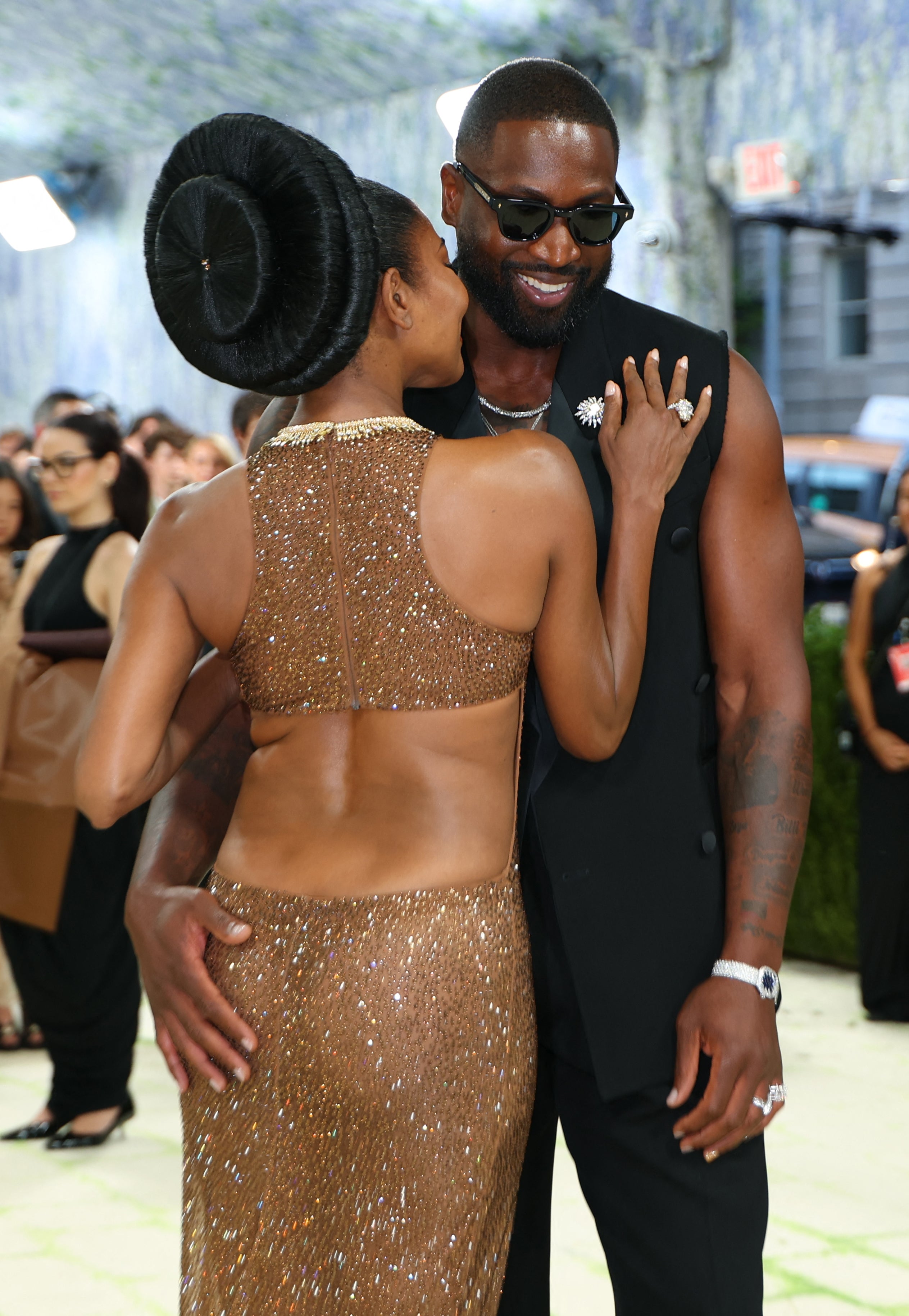 A pistillate   successful  a sparkling gown hugs a antheral   successful  a sleeveless suit   connected  a manner  lawsuit   reddish  carpet