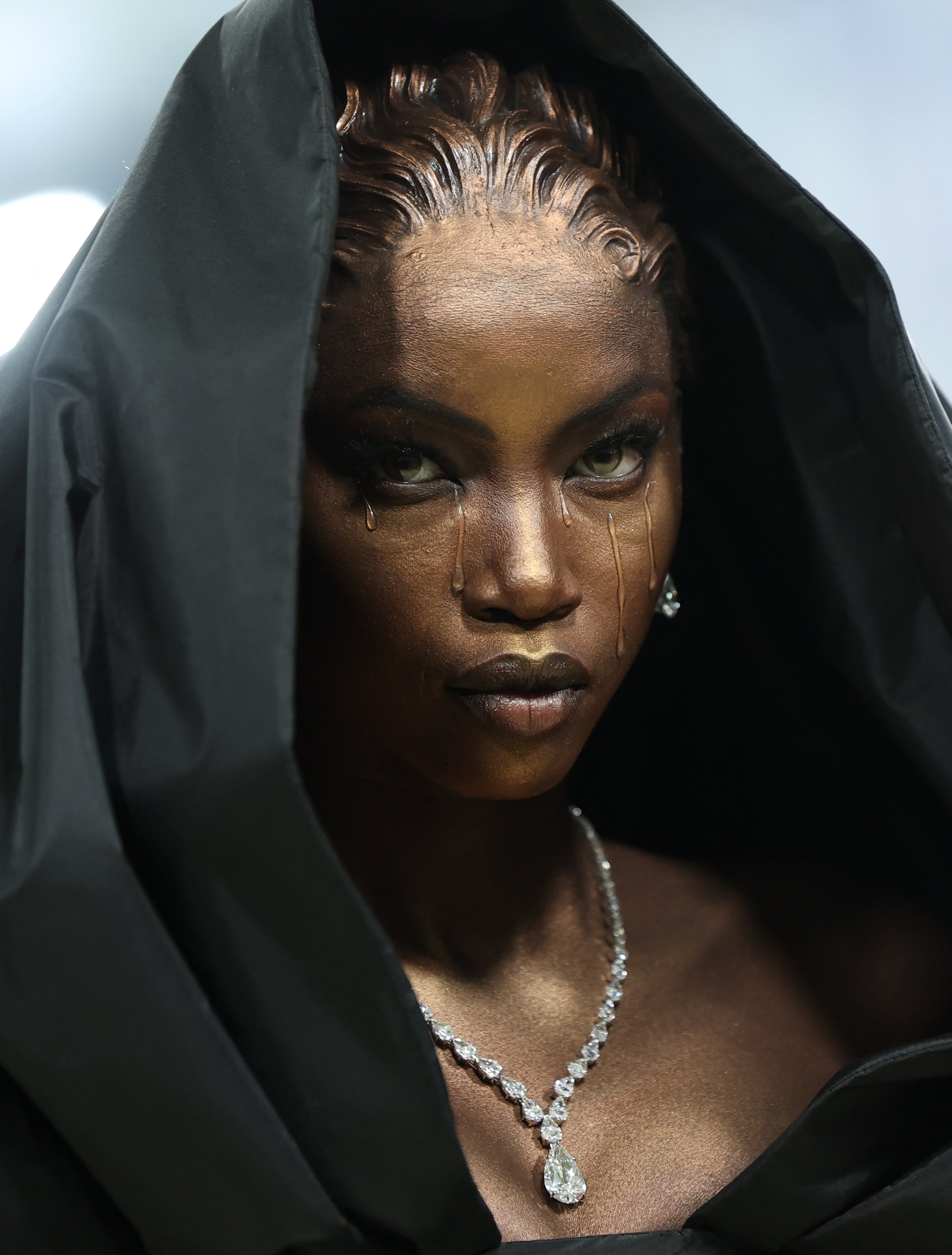 Model successful  a melodramatic  hooded outfit with metallic constitution  and a diamond necklace, posing with an aggravated  expression