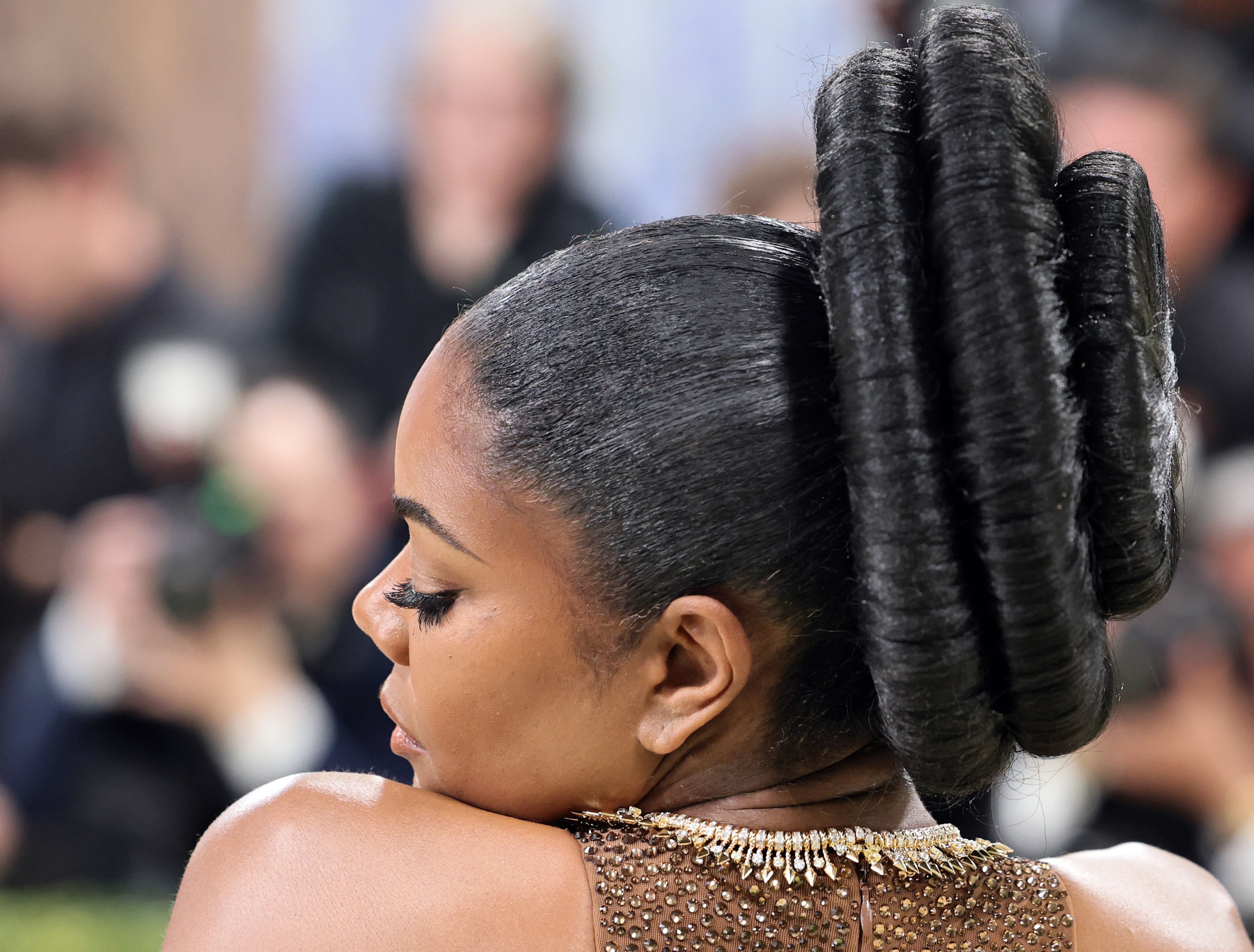 Person with sleek braided hairstyle facing away, wearing a formal  adorned with sparkling embellishments