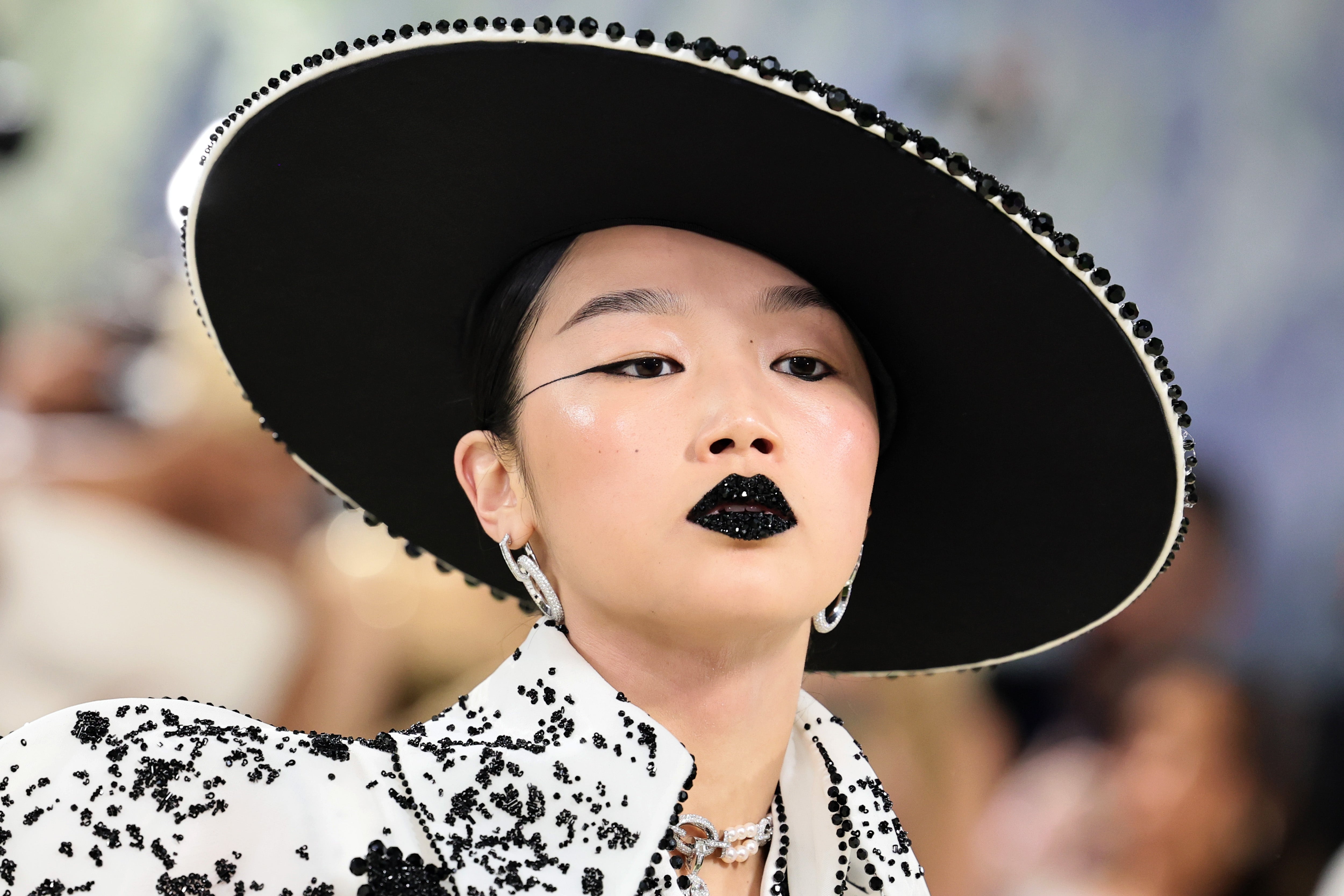 Person wearing a large, embellished chapeau  and achromatic  sequined lips astatine  a high-fashion event, with sparkling attire