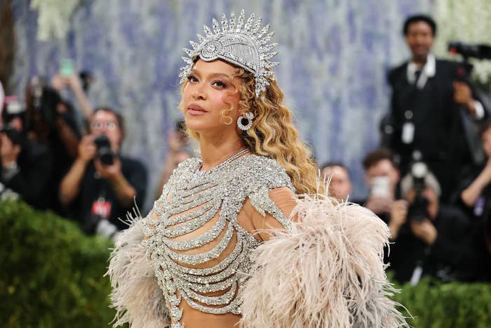 Celebrity successful  feather and crystal gown, wearing decorative headpiece, poses connected  the reddish  carpet. Photographers successful  the background