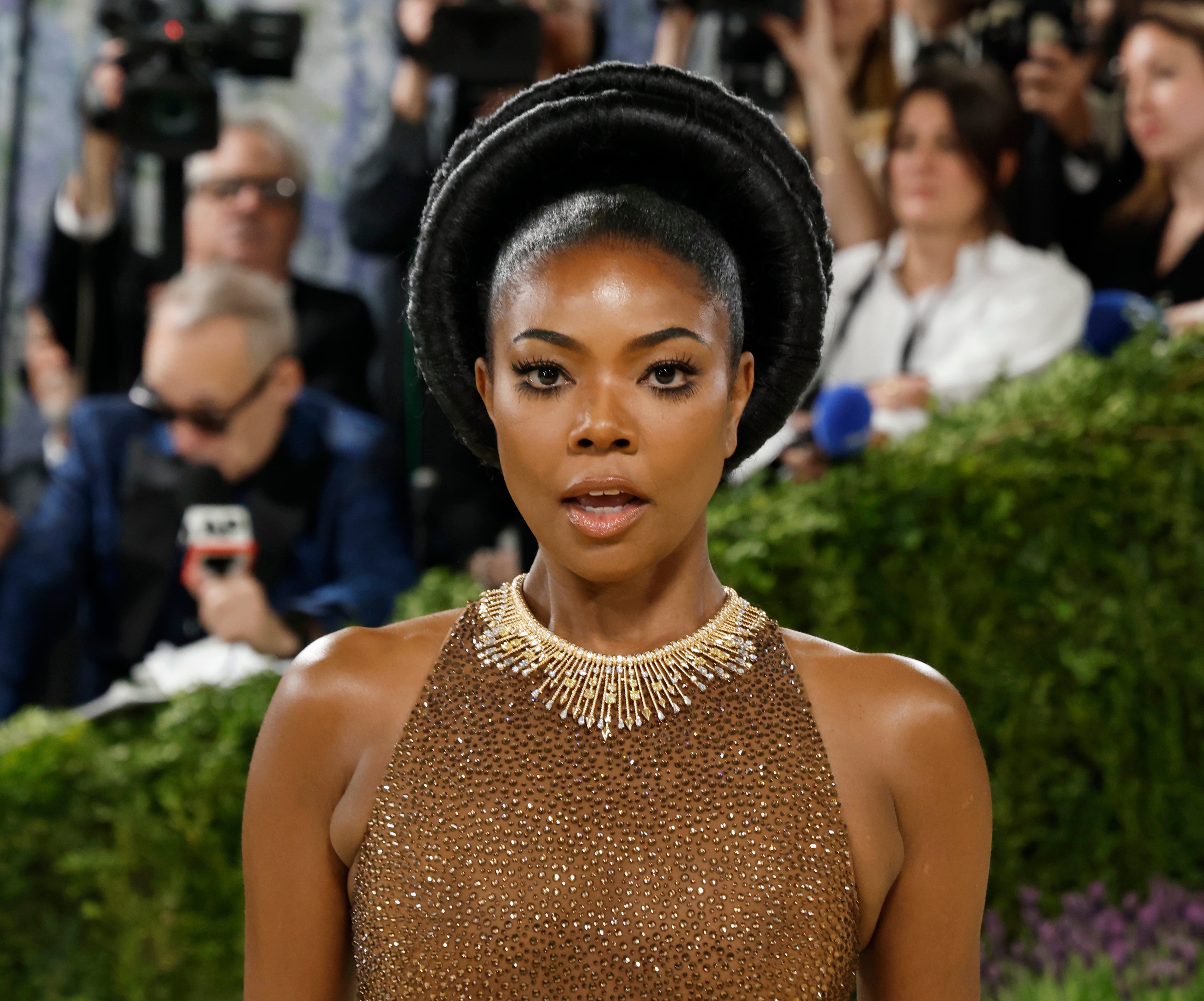Person successful  a textured gown with a beaded neckline astatine  an event, surrounded by photographers and greenery successful  the background