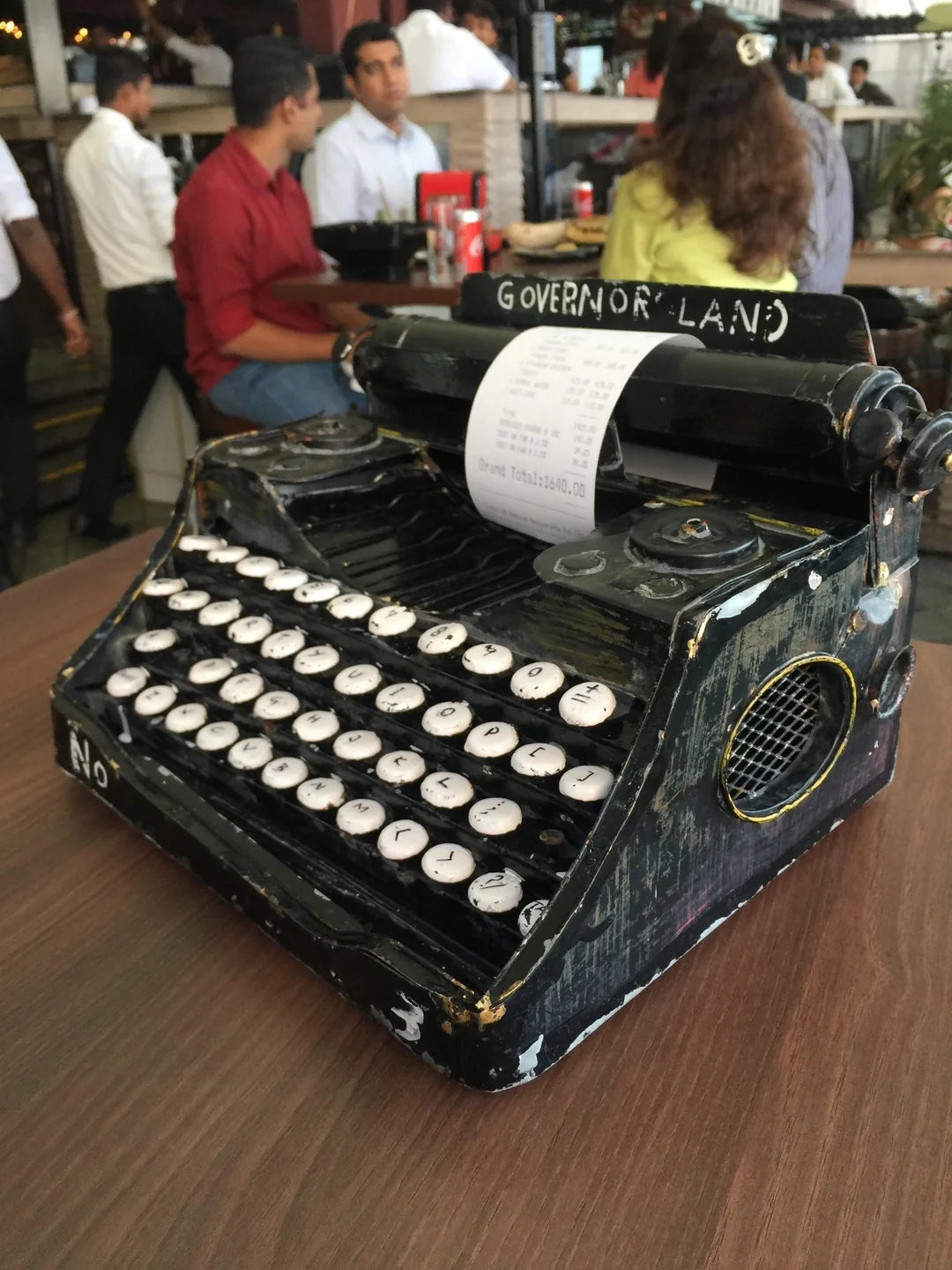 Vintage typewriter converted into a bill holder on a wooden table in a busy café setting