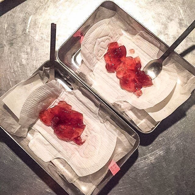 Two sanitary pads on trays with spoons, topped with a red, jam-like substance