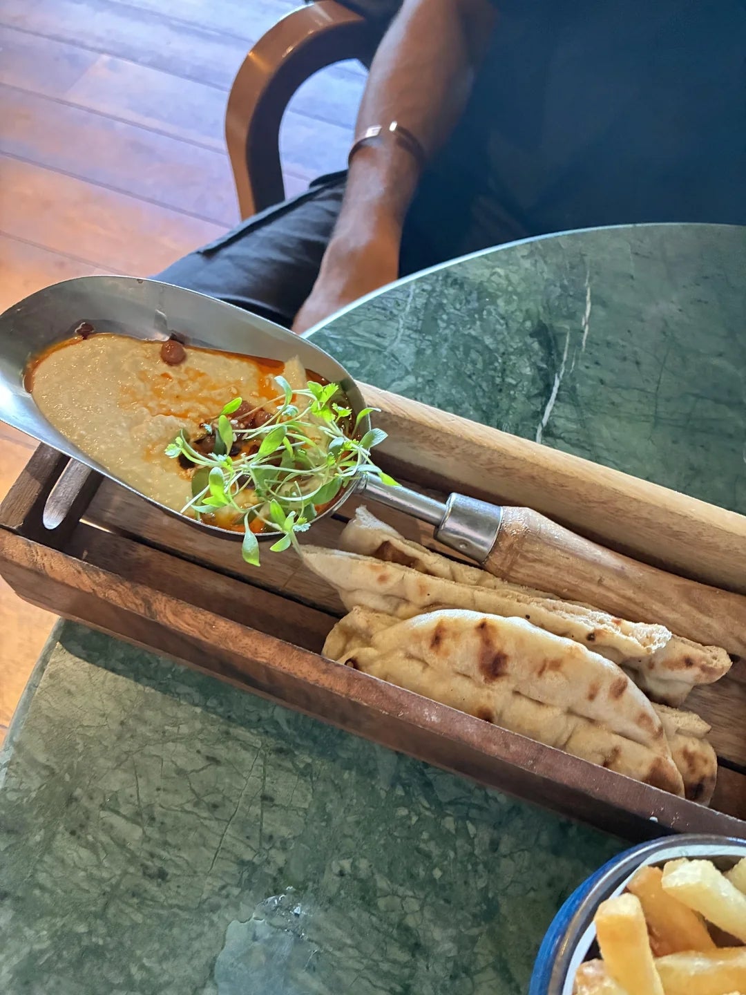 A platter with hummus topped with sprouts, served with pita bread on a wooden board