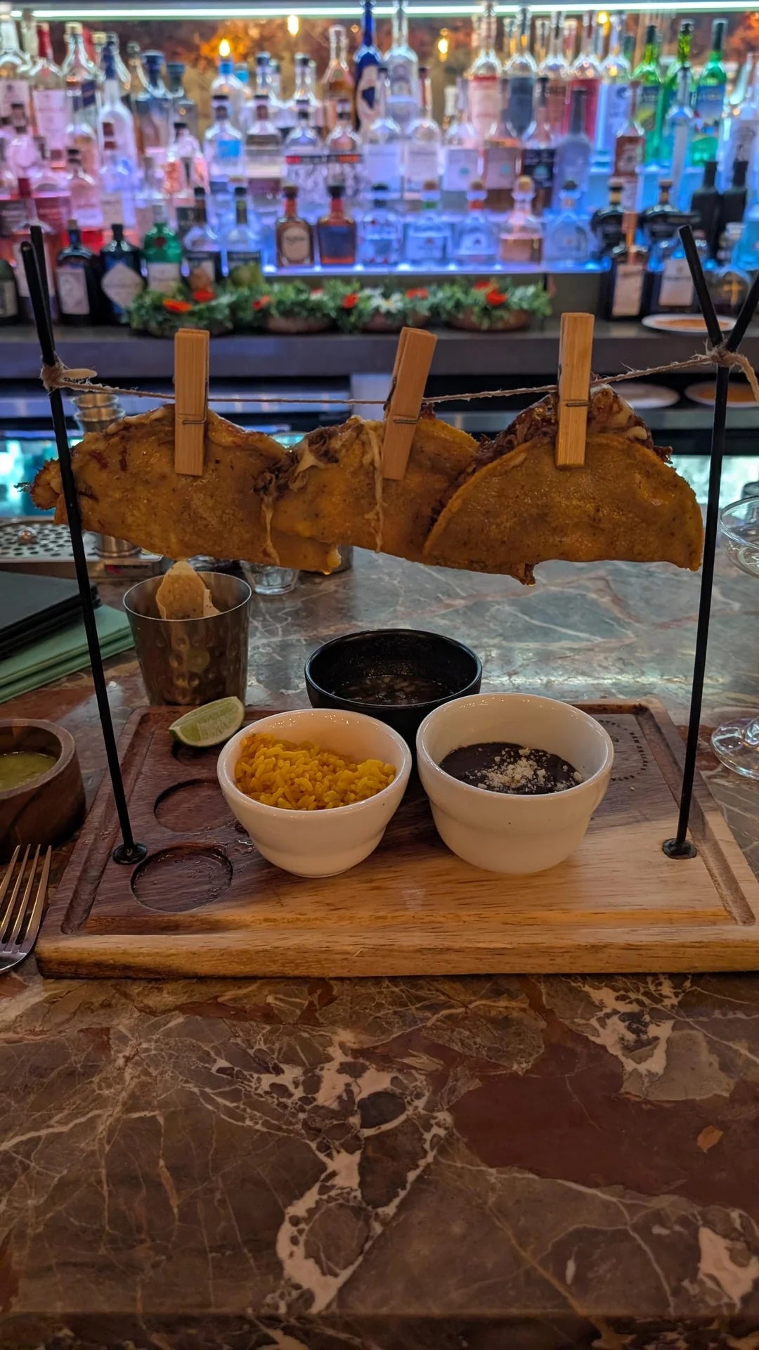 Tacos displayed on a rack with small bowls of rice and beans on a wooden board, set on a restaurant table