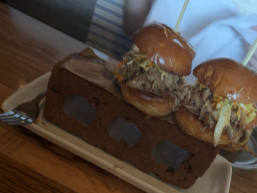 Two pulled pork sliders with coleslaw skewered on top of a hollow brick-like base on a plate