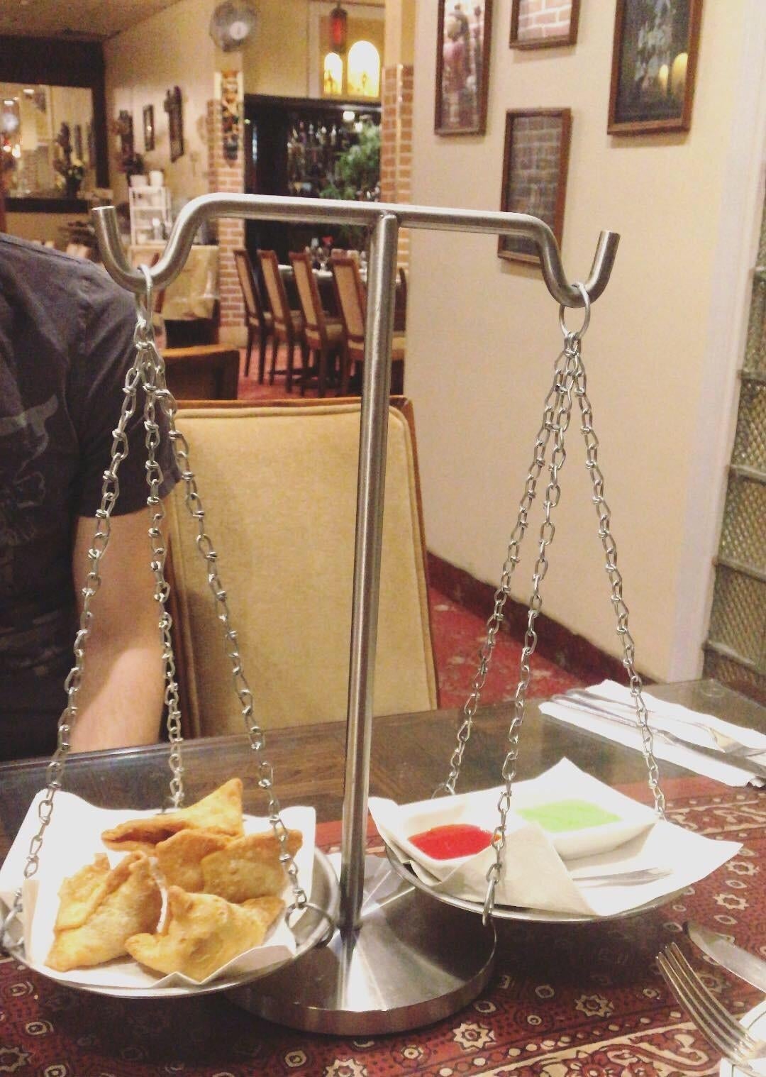 Scale-shaped serving tray with samosas and sauces on small plates in a restaurant. Dining table setting with a person partially visible