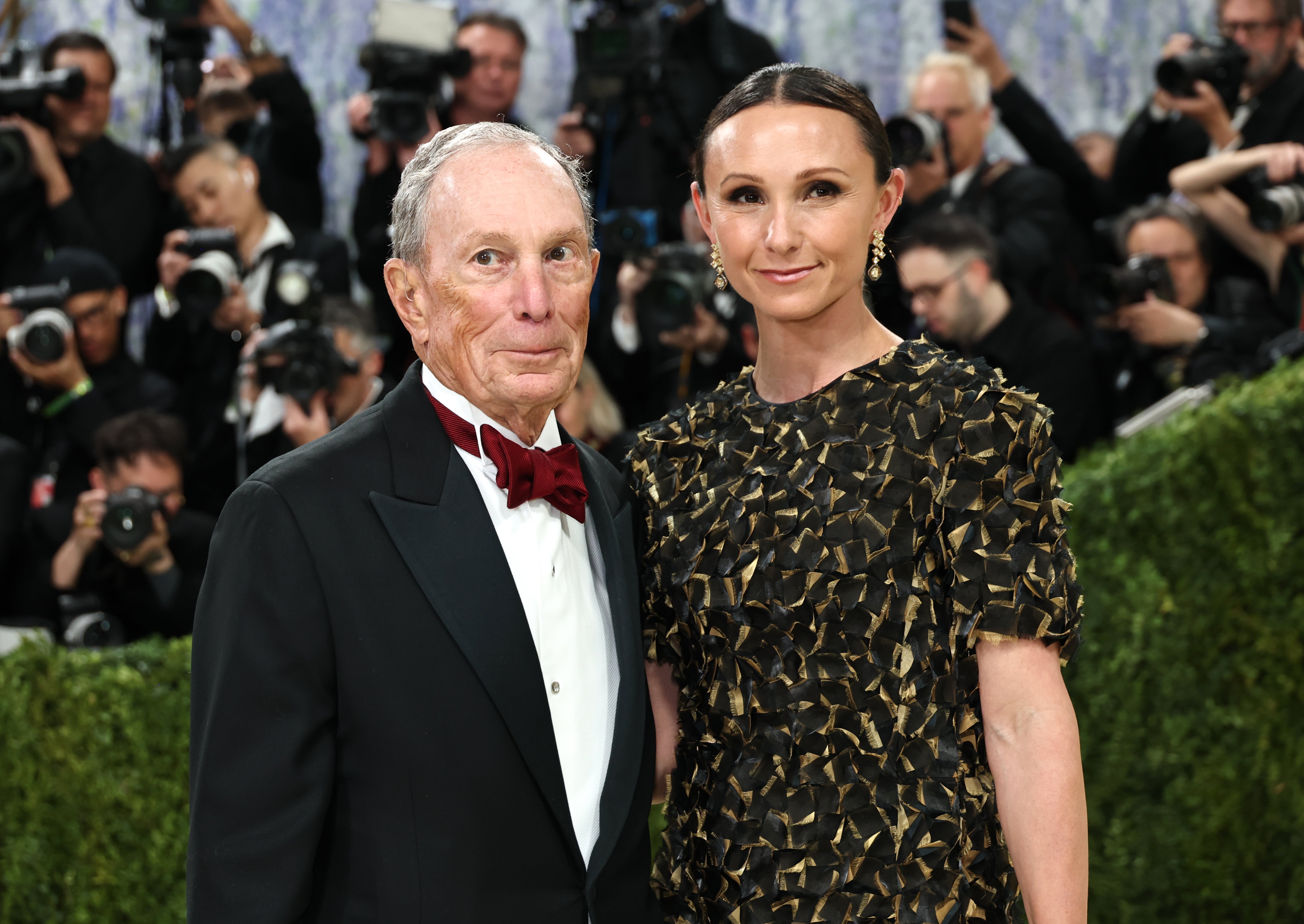 A antheral   successful  a tuxedo with a bow necktie  and a pistillate   successful  an elegant patterned gown airs  connected  the reddish  carpet, surrounded by photographers