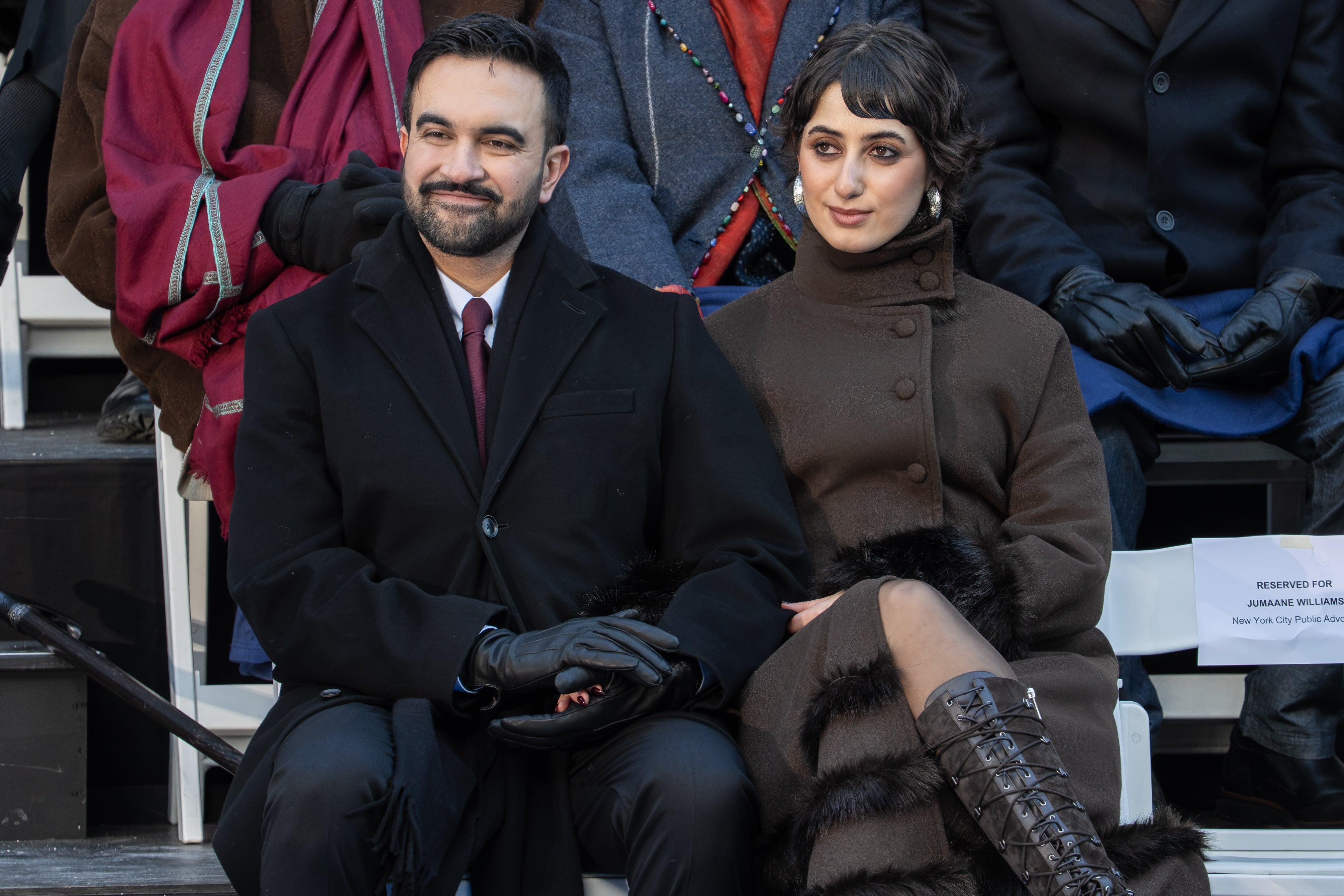 Two individuals seated astatine  an event. The pistillate   wears a long, elegant overgarment  and patterned boots; the antheral   is successful  a ceremonial  suit   and gloves