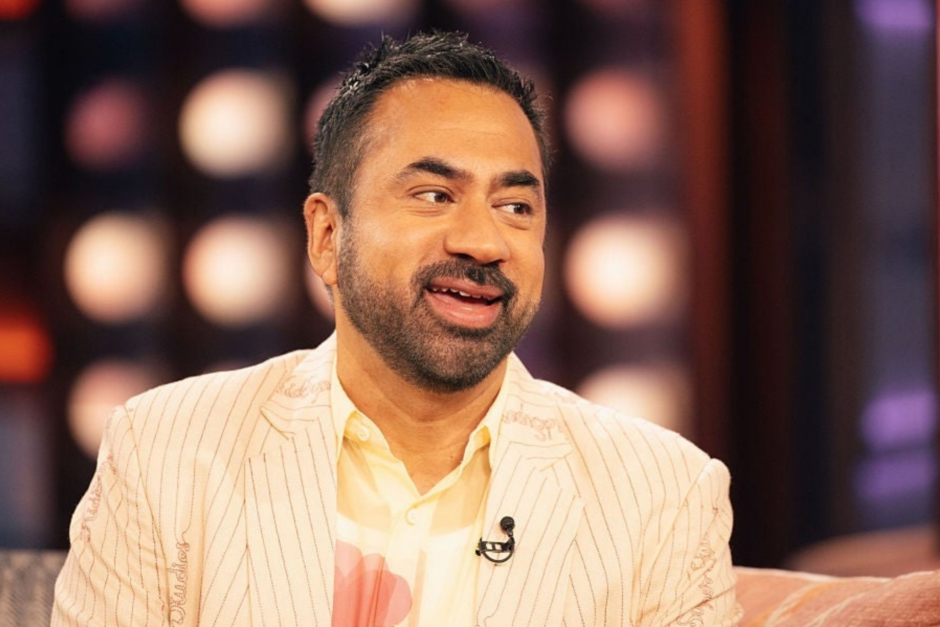 Person successful  a patterned suit   with an open-collared shirt, seated and speaking successful  a well-lit workplace  setting