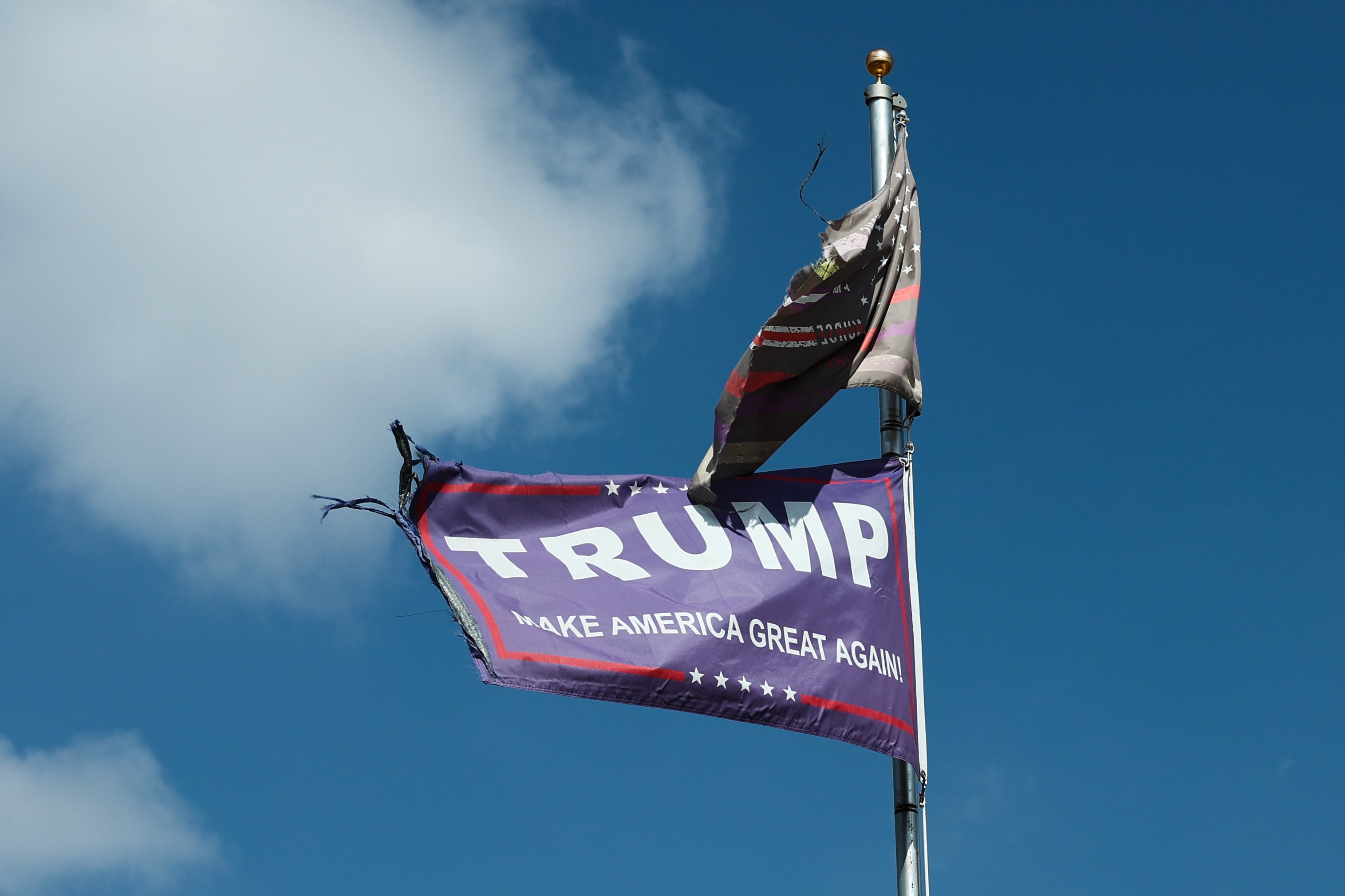 "Tattered 'Make America Great Again' emblem  connected  a rod  against a bluish  sky."