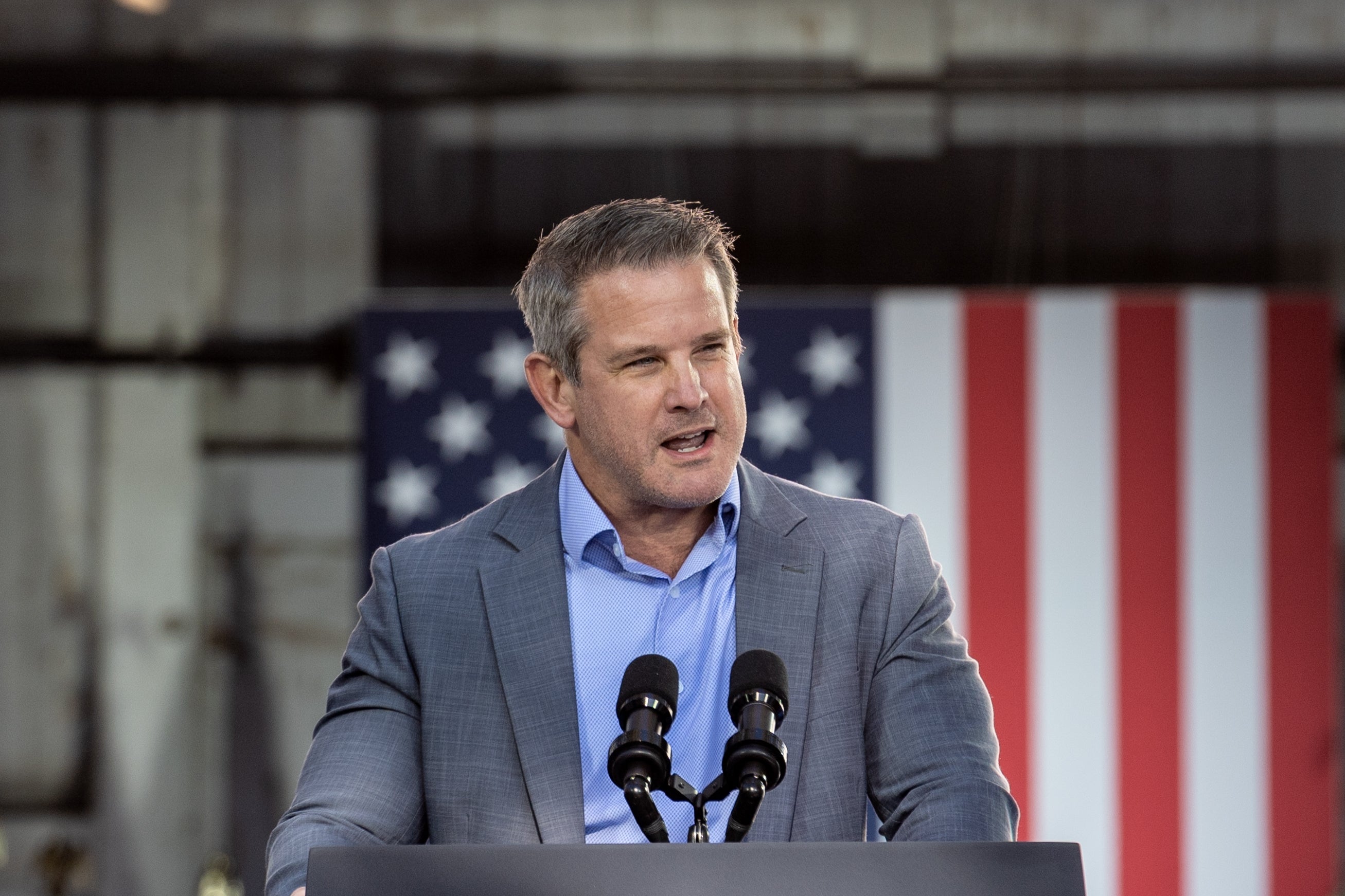 A idiosyncratic   successful  a grey  suit   speaks astatine  a podium with microphones, lasting  successful  beforehand   of a ample  U.S. emblem  backdrop