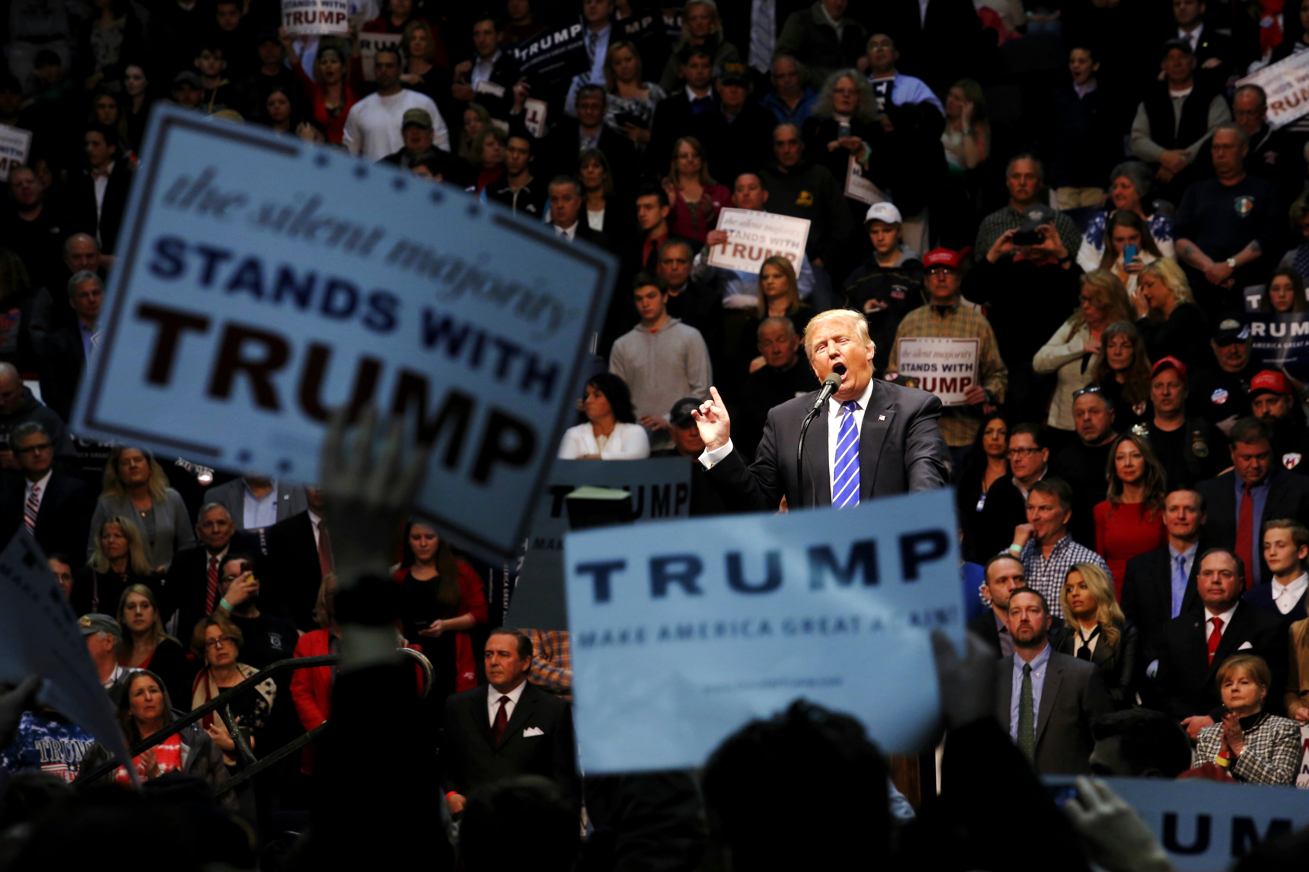 Large assemblage  astatine  a rally, idiosyncratic   astatine  the podium gestures, surrounded by supporters holding pro-campaign signs