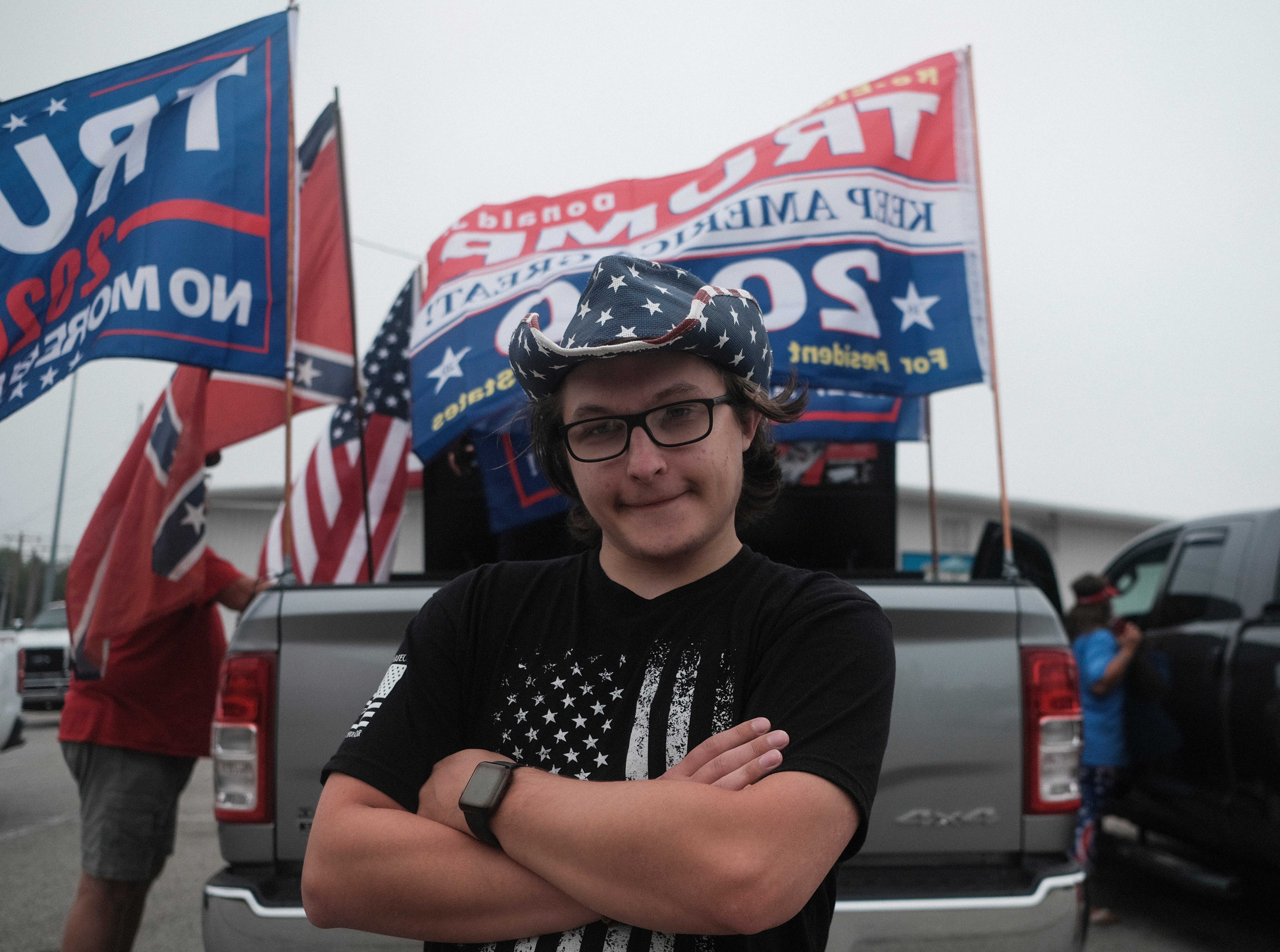 Person successful  a star-patterned headdress  and flag-themed garment  poses successful  beforehand   of vehicles with governmental  flags and signs