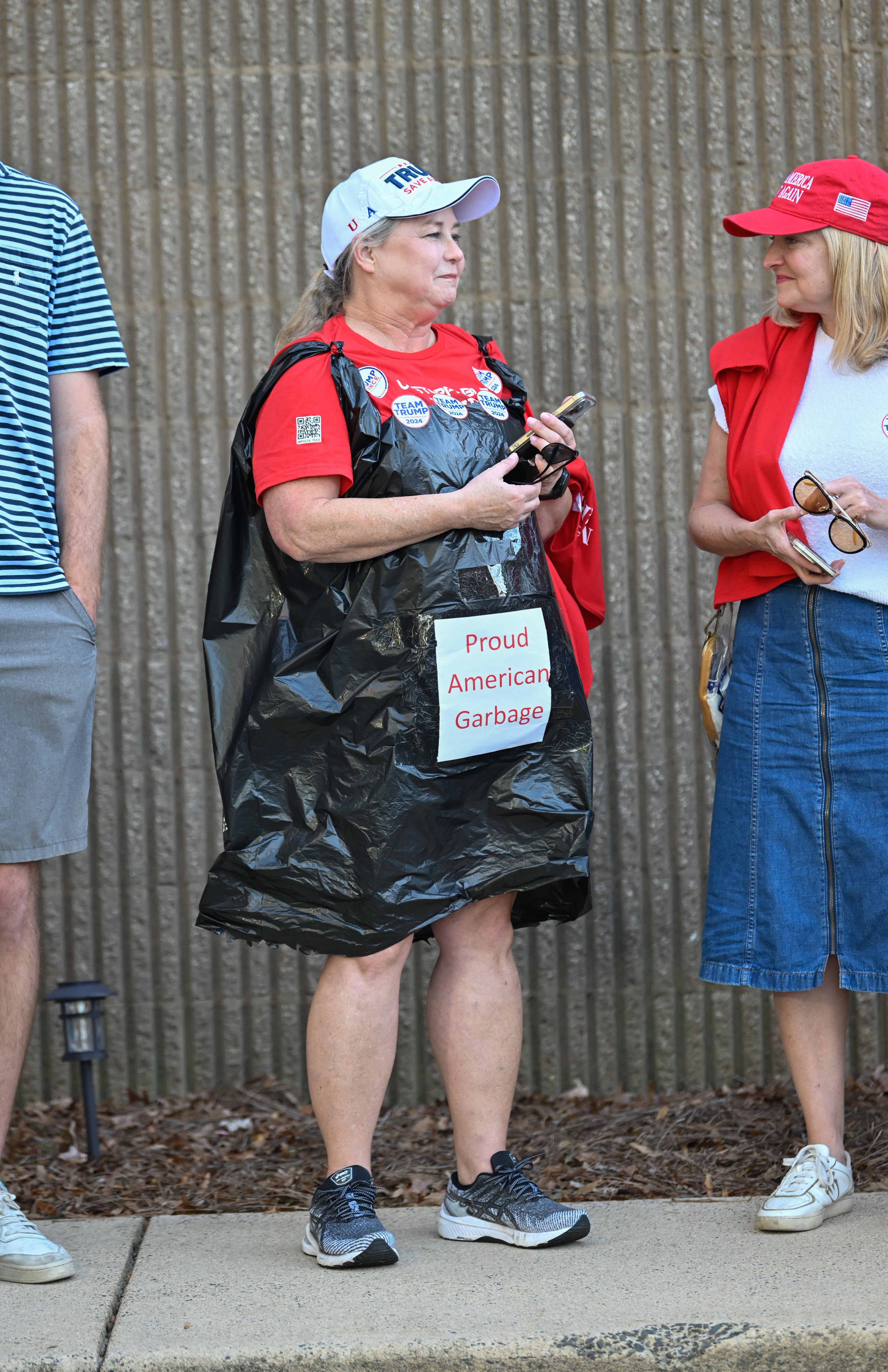 Person wearing a motion   speechmaking  "Proud American Garbage" and a garbage container  astatine  a nationalist   event, conversing with different  individual