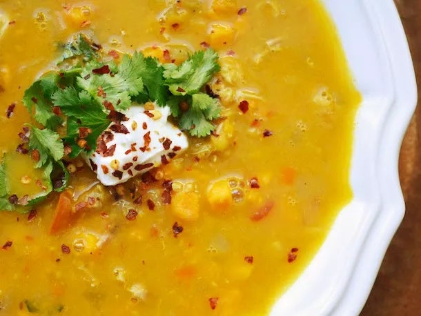 A bowl of thick soup topped with cilantro, sour cream, and red pepper flakes, containing visible chunks of vegetables