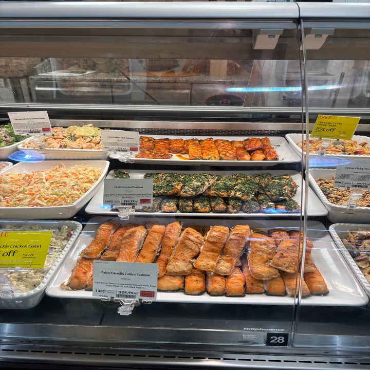 Deli counter displaying a variety of prepared foods, including salmon and slaws