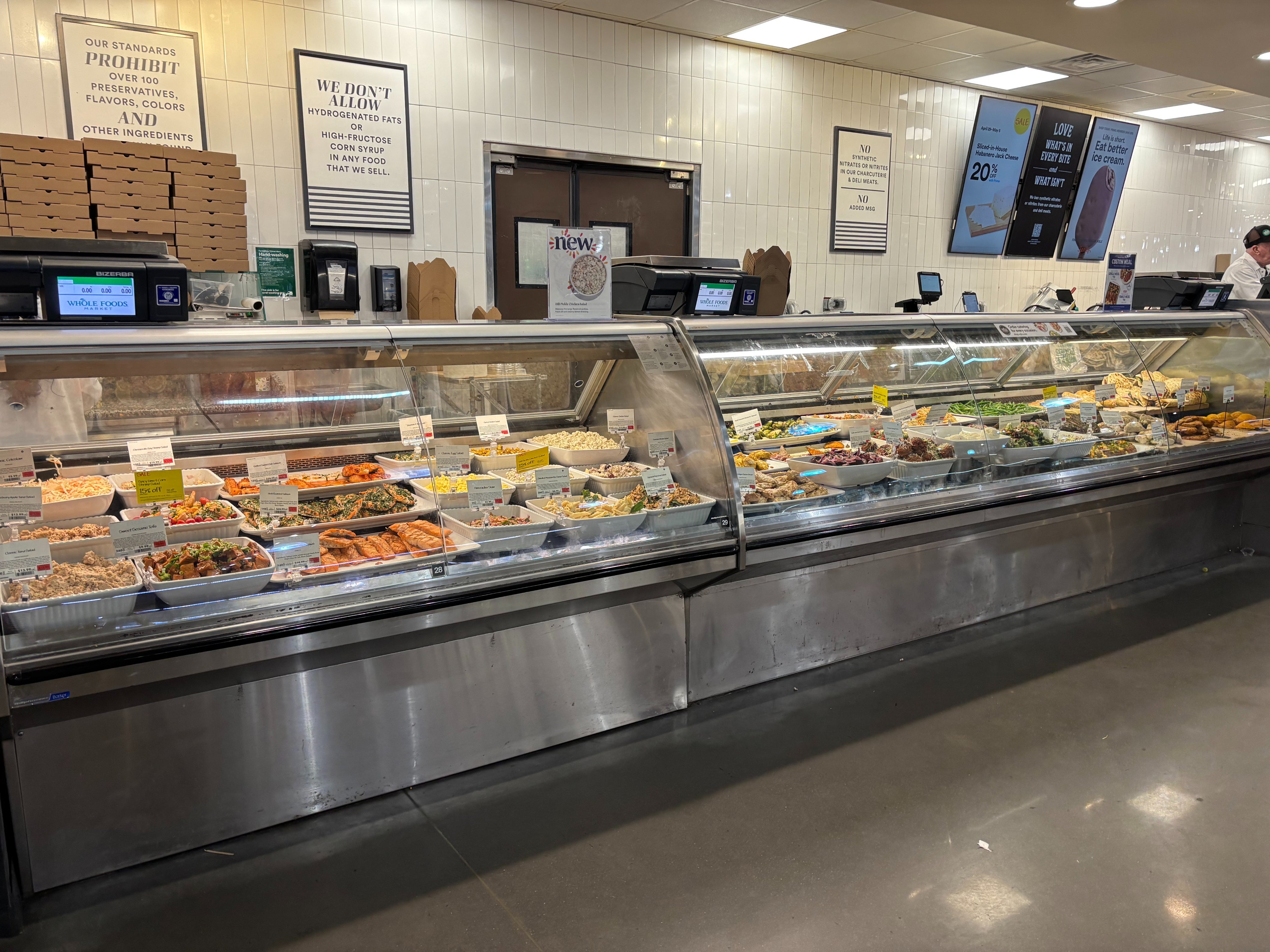Grocery store deli counter displaying various prepared foods in trays under a glass case