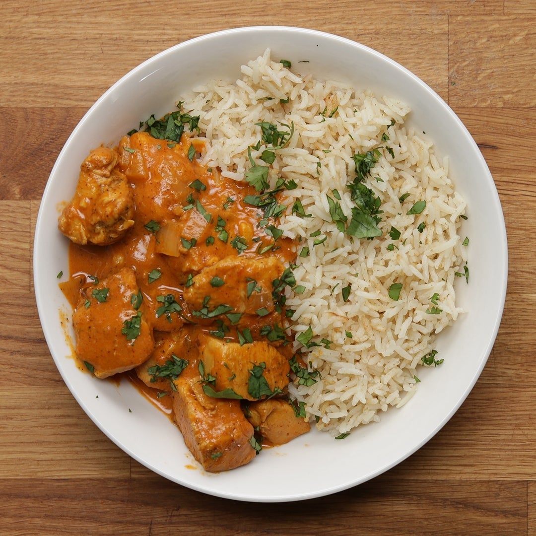 A plate featuring chicken tikka masala with a creamy sauce on one side and fluffy white rice garnished with herbs on the other