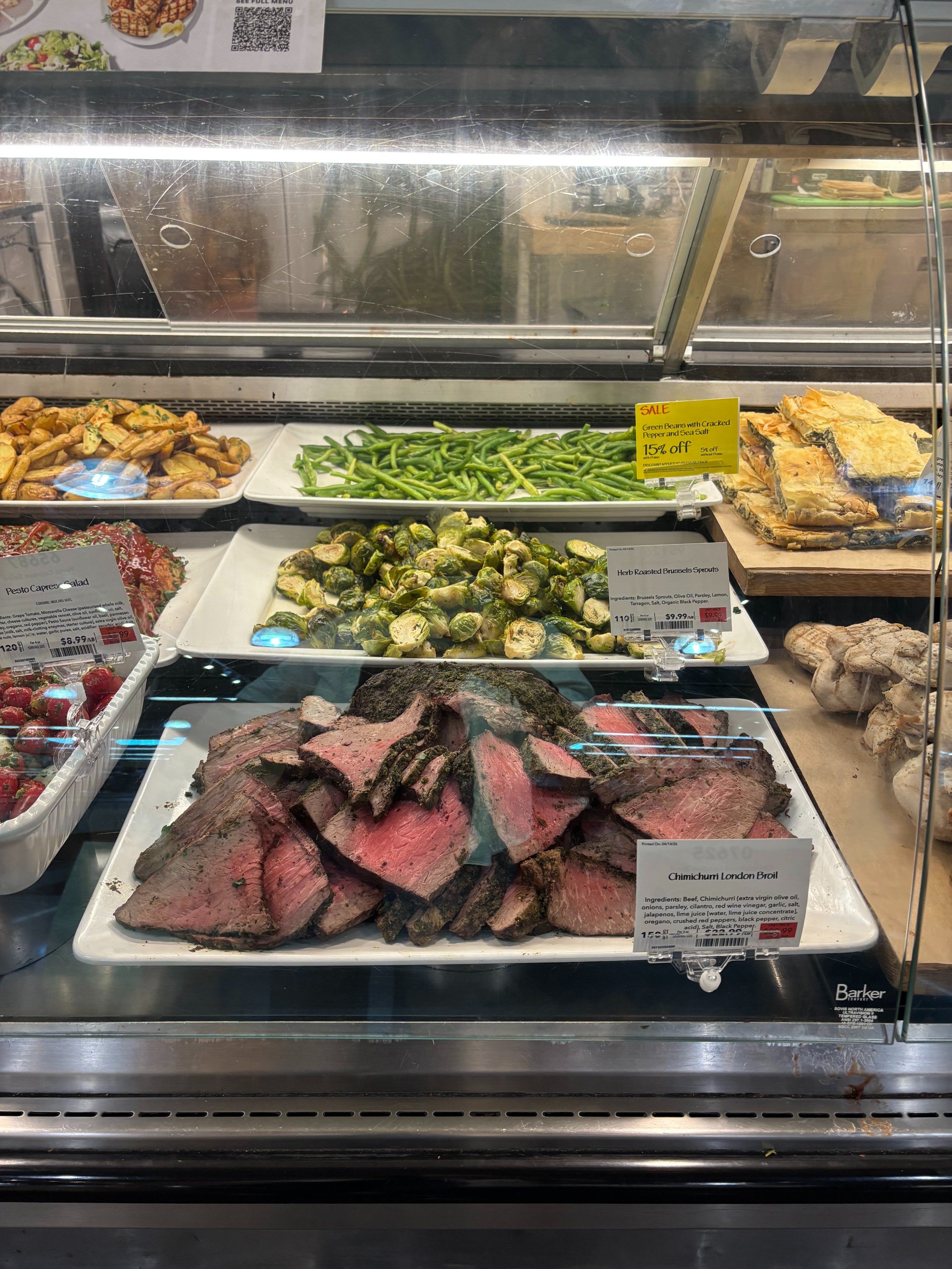 Deli display with sliced roast beef, roasted Brussels sprouts, green beans, and other prepared foods