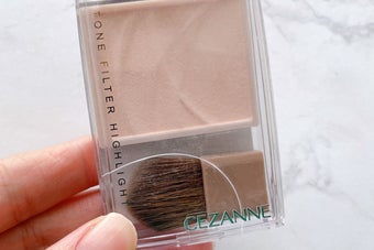 CEZANNEのハイライトパウダーを持つ手。小さなブラシ付きのコンパクト。