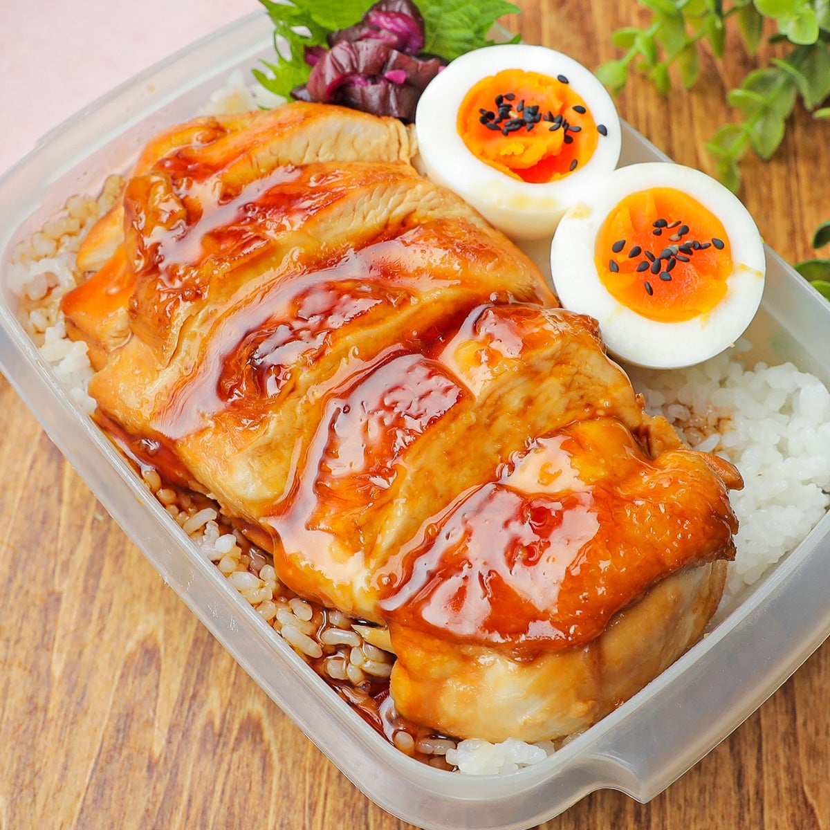 ご飯の上にソースがかかった照り焼きチキンと半熟卵が乗った弁当。卵には黒ごまが散らしてある。