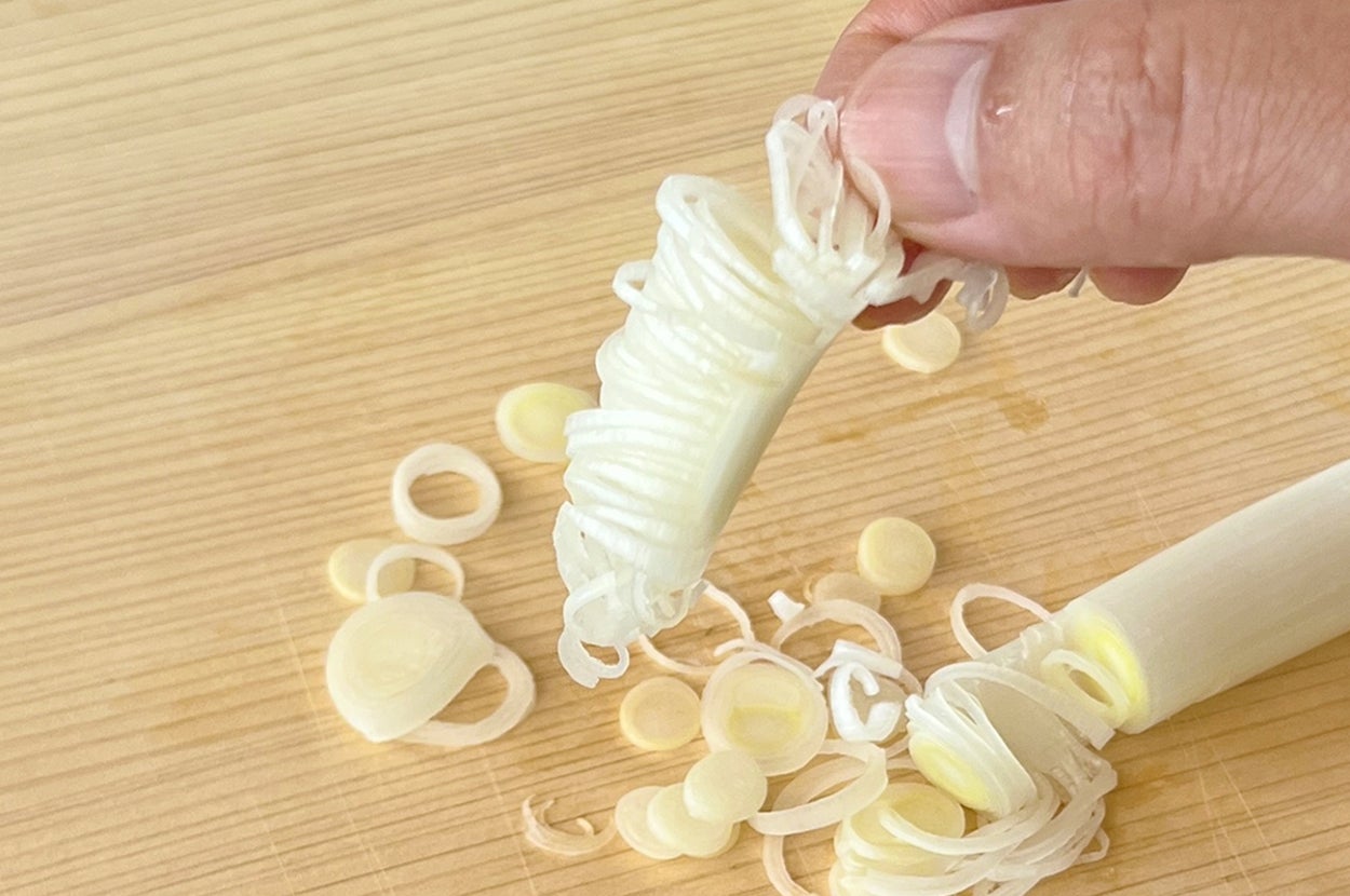 手でネギを切っている様子。まな板の上にスライスされたネギが散らばっています。