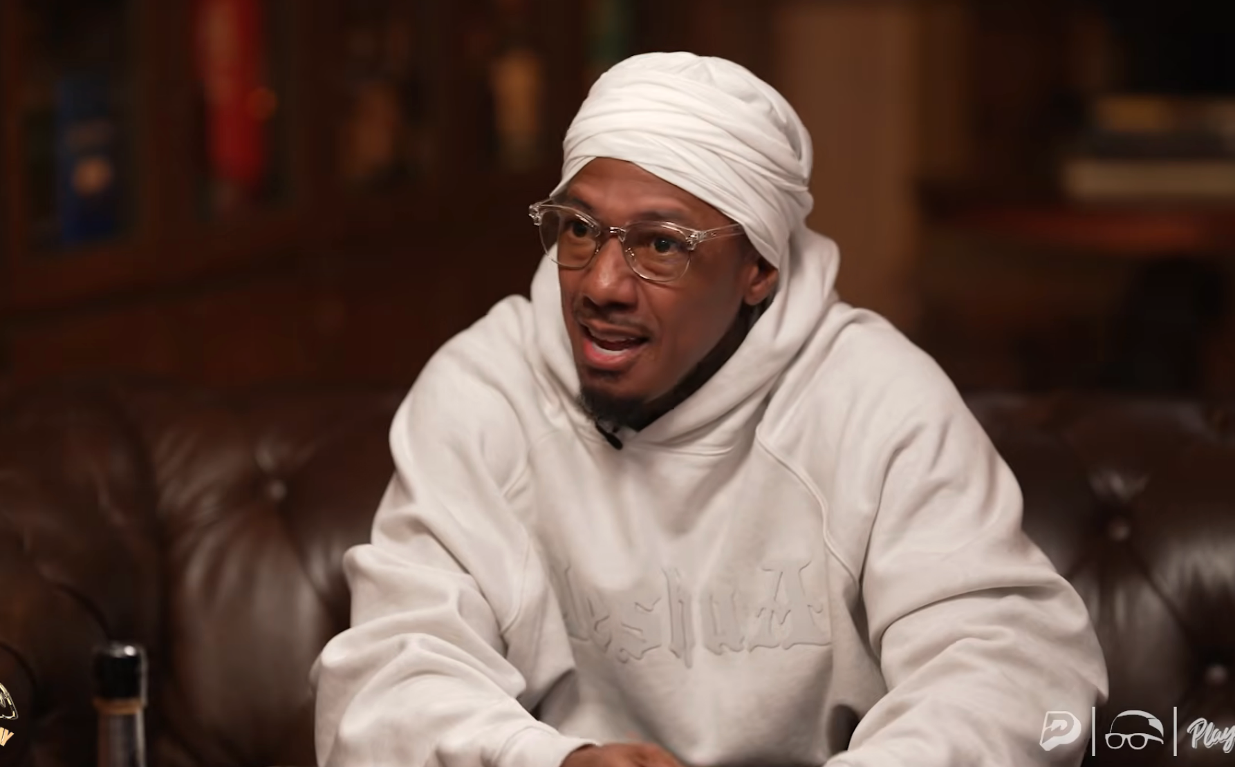 Person seated connected  a leather sofa wearing a achromatic  hoodie and headwrap, speaking during an interview