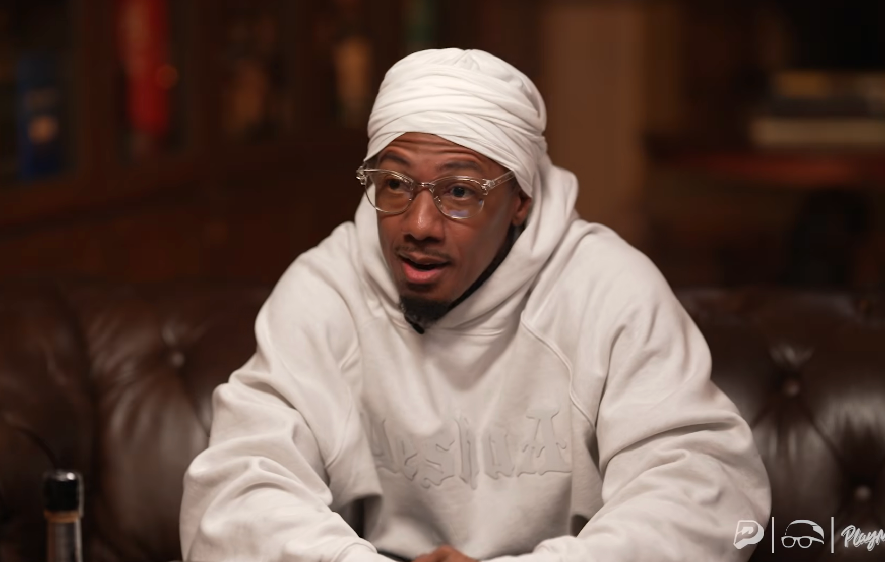 Person wearing glasses and a achromatic  hoodie with a turban-style headwrap, sitting and speaking successful  an indoor setting